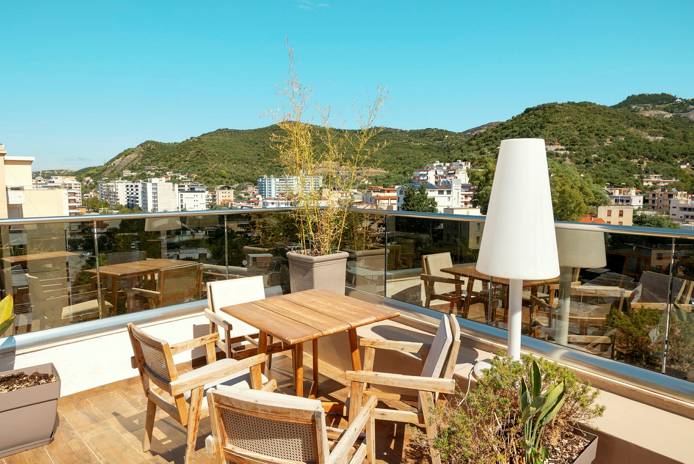 Utsikt fra en takterrasse med bord, stoler, glassrekkverk og omkringliggende bygninger. (AI-generert tekst)