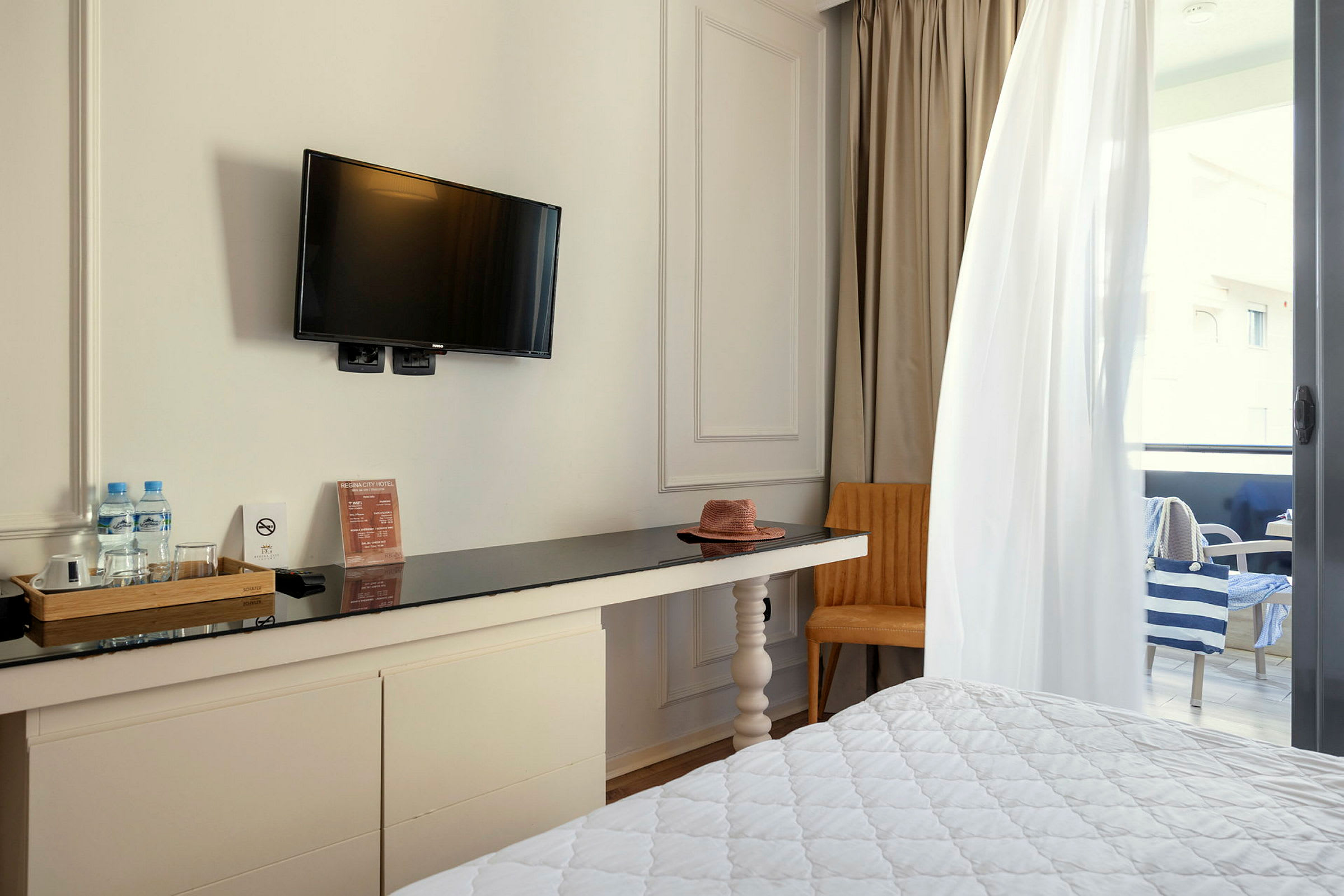 Hotellrom med TV på veggen, skrivebord, stol og delvis synlig balkong. (AI-generert tekst)