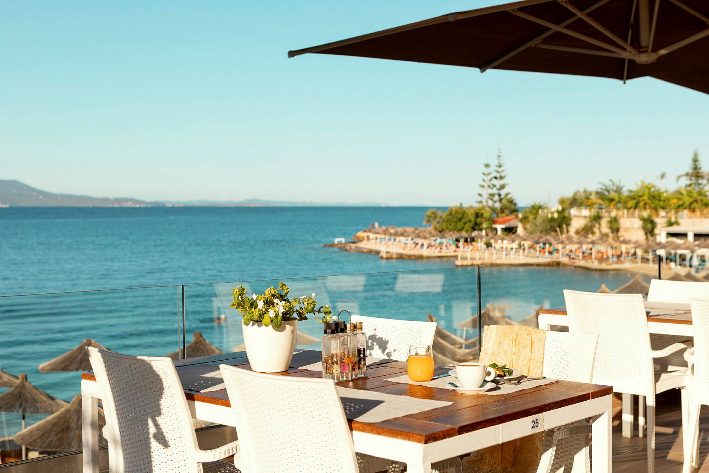 Utsikt over havet fra en restaurantterrasse med hvite bord og stoler. (AI-generert tekst)
