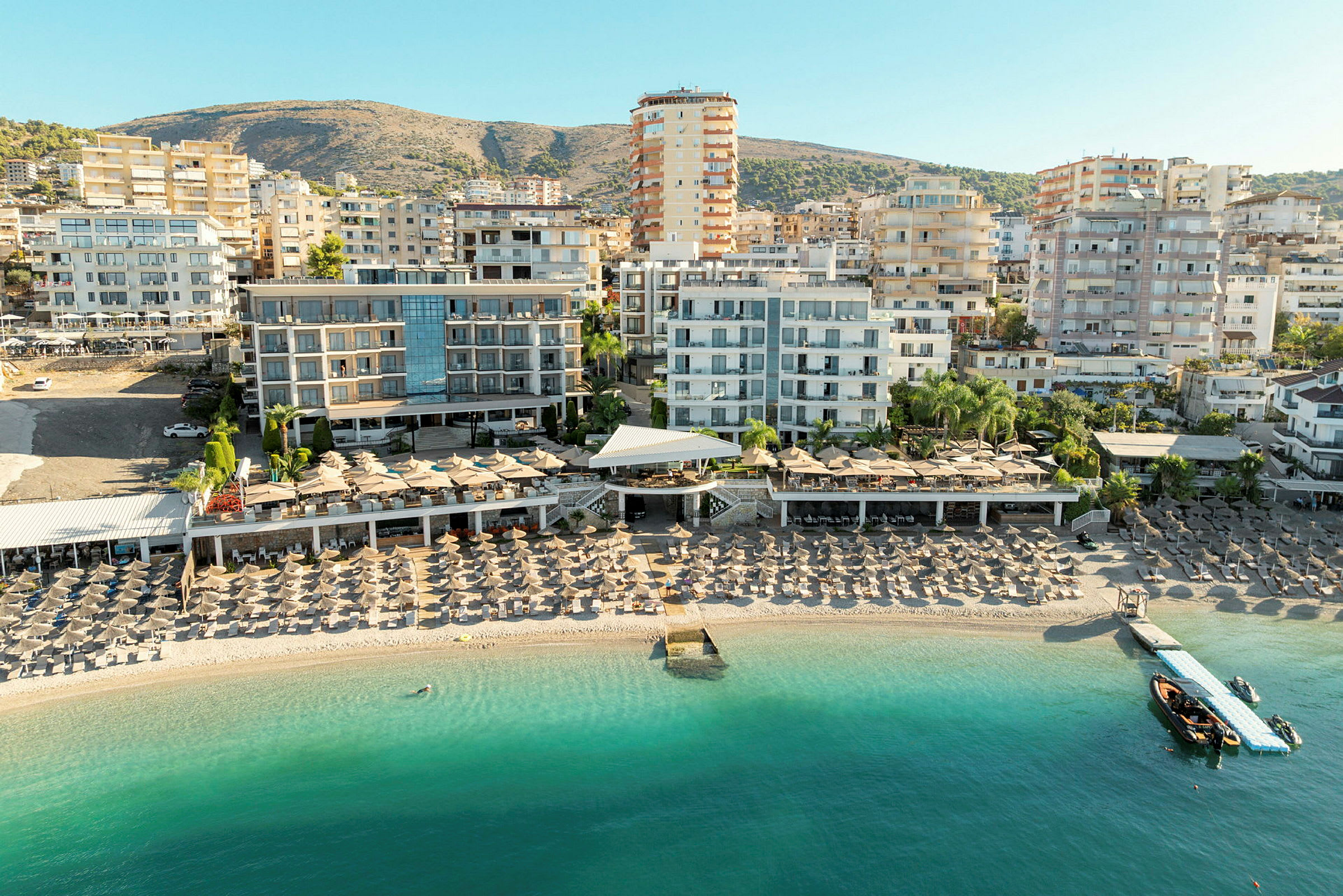 Utsikt over en strand med solsenger og hotellbygninger i bakgrunnen. (AI-generert tekst)