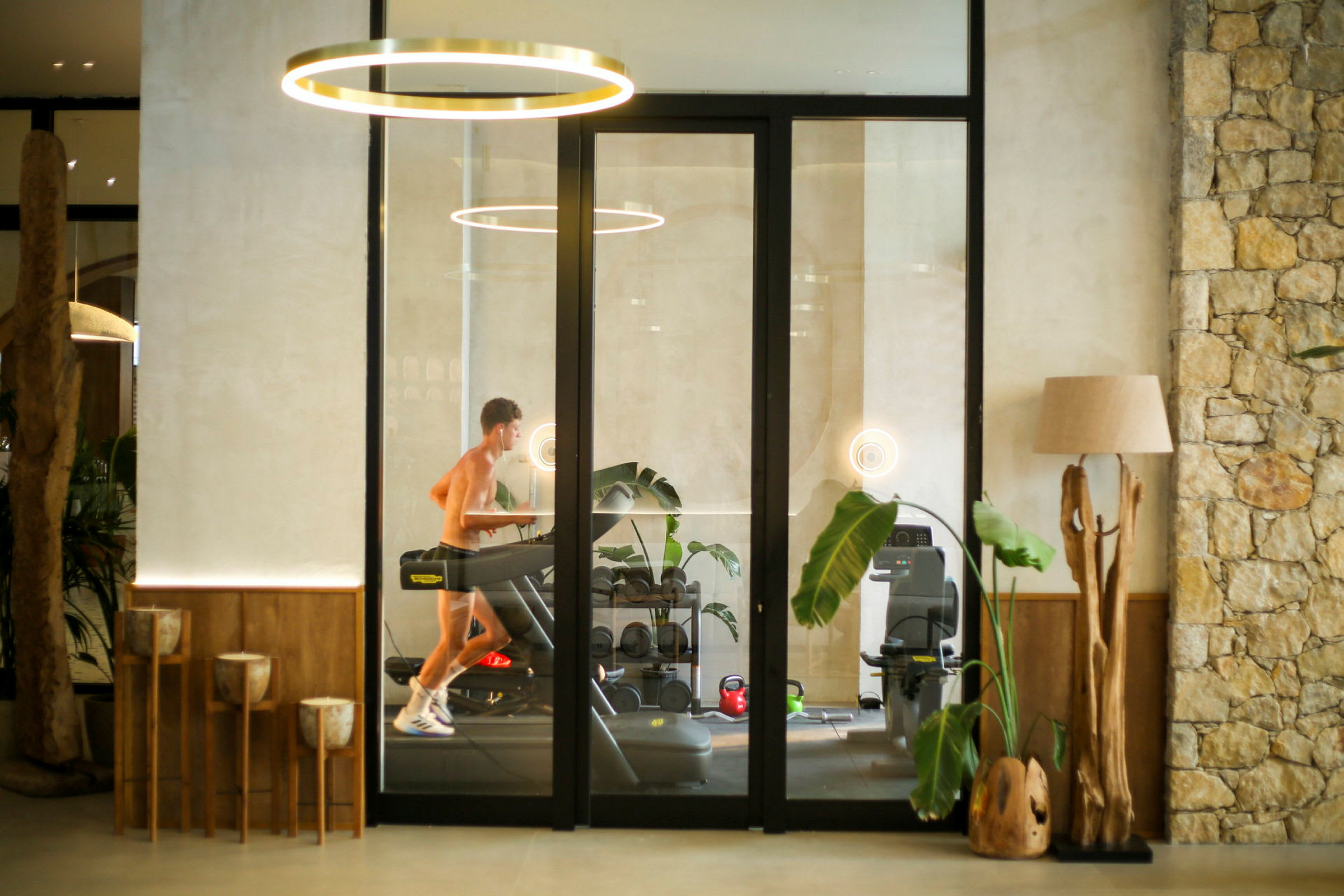 En person løper på en tredemølle i et moderne treningsstudio med planter og dekorative trefunksjoner. (AI-generert tekst)
