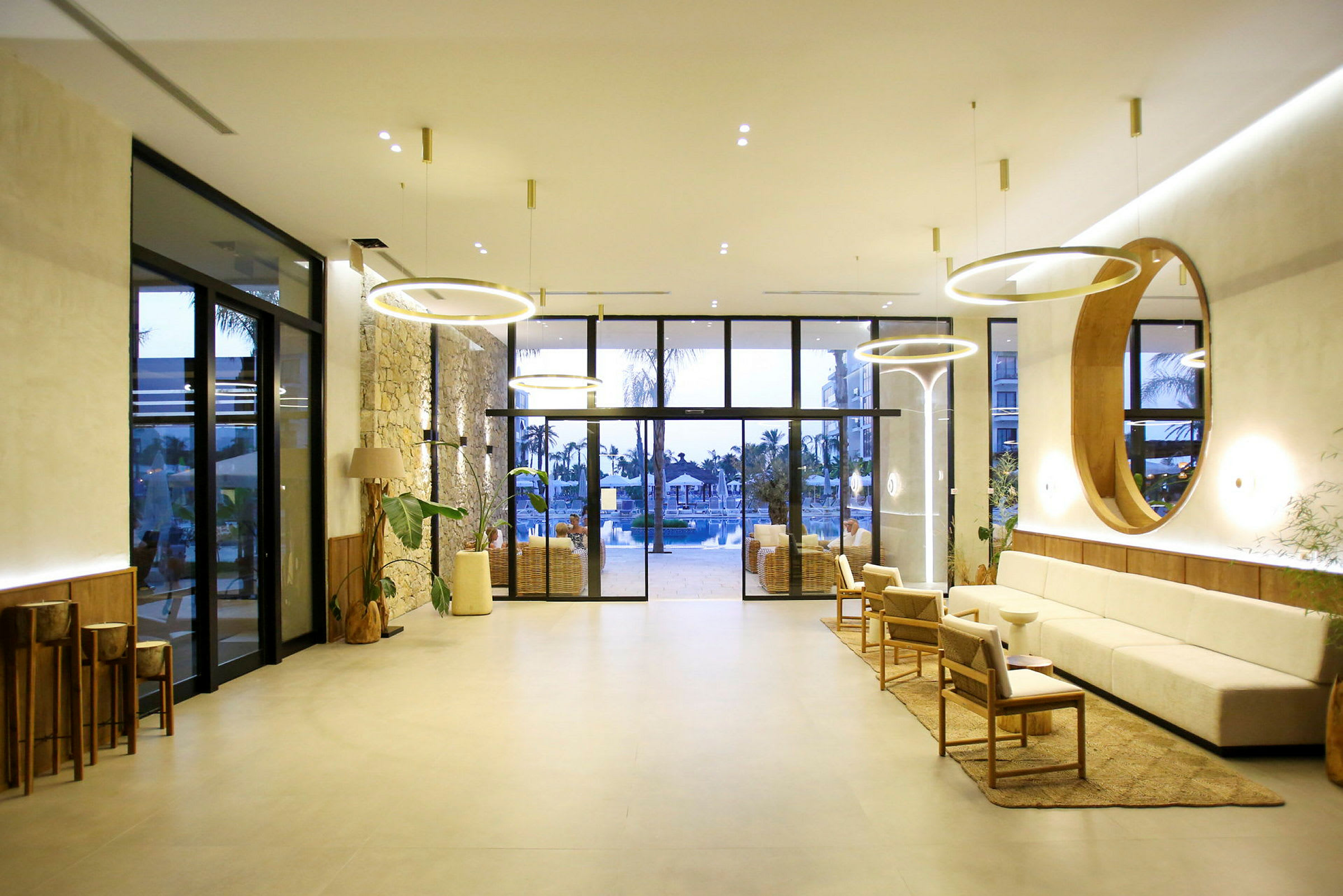 Et moderne hotellobbyområde med komfortable sitteplasser, stilige lamper og store glassdører som fører til et bassengområde. (AI-generert tekst)