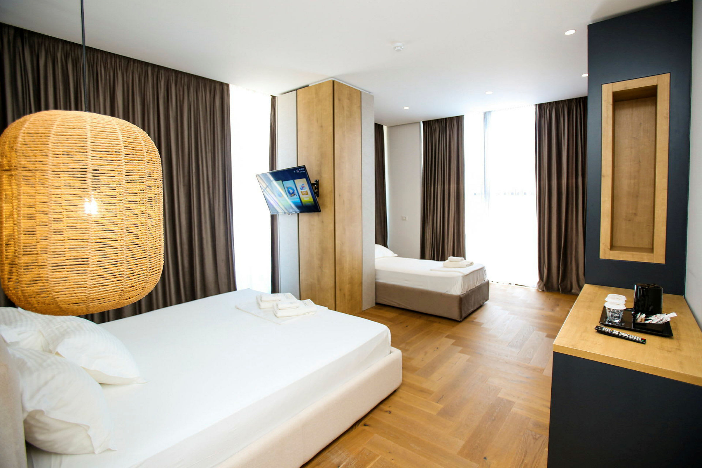Et hotellrom med to senger, en hengende lampe, en veggmontert TV og et skrivebord med en kaffetrakter. (AI-generert tekst)