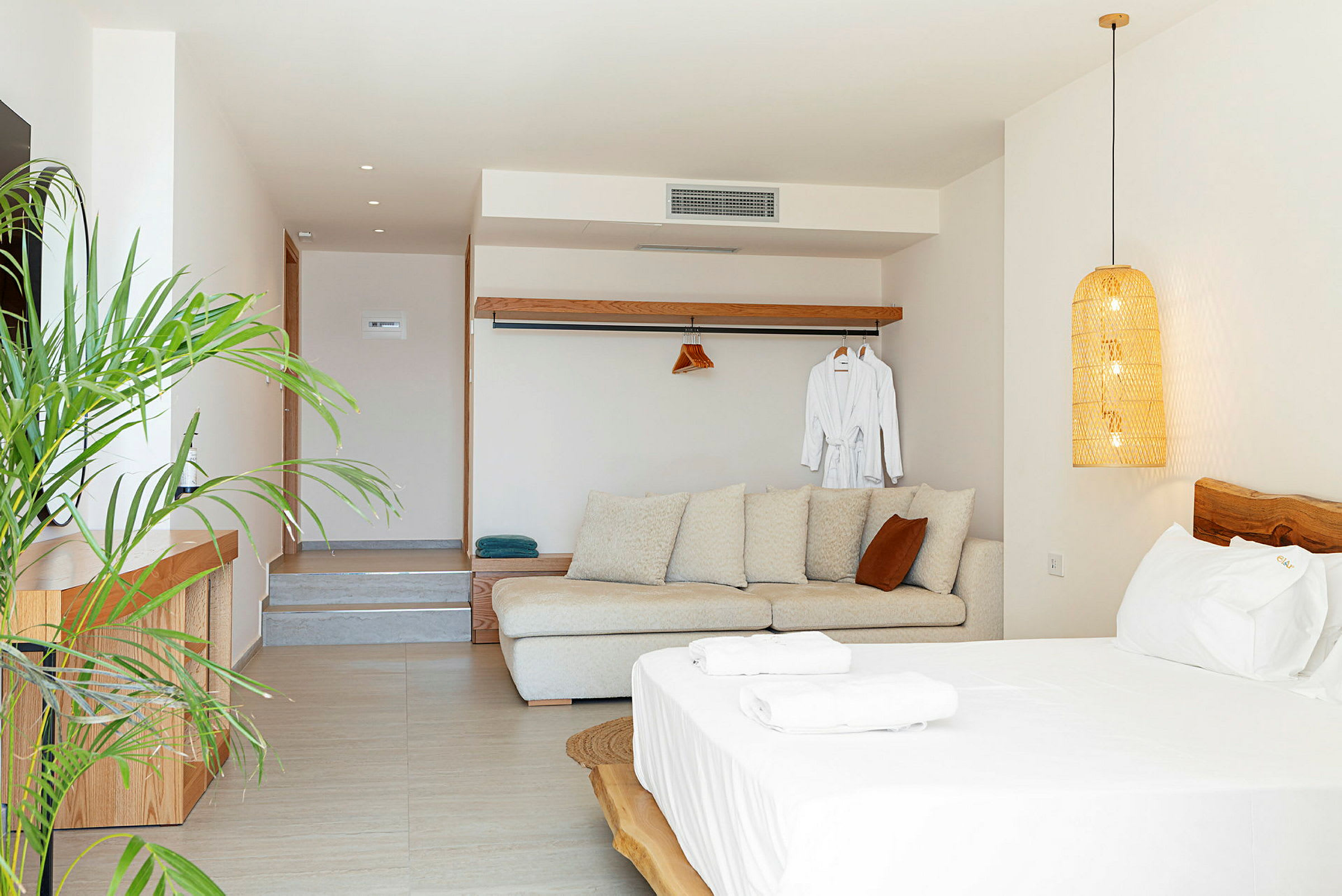 Et lyst og moderne hotellrom med sofa, seng og planter. (AI-generert tekst)