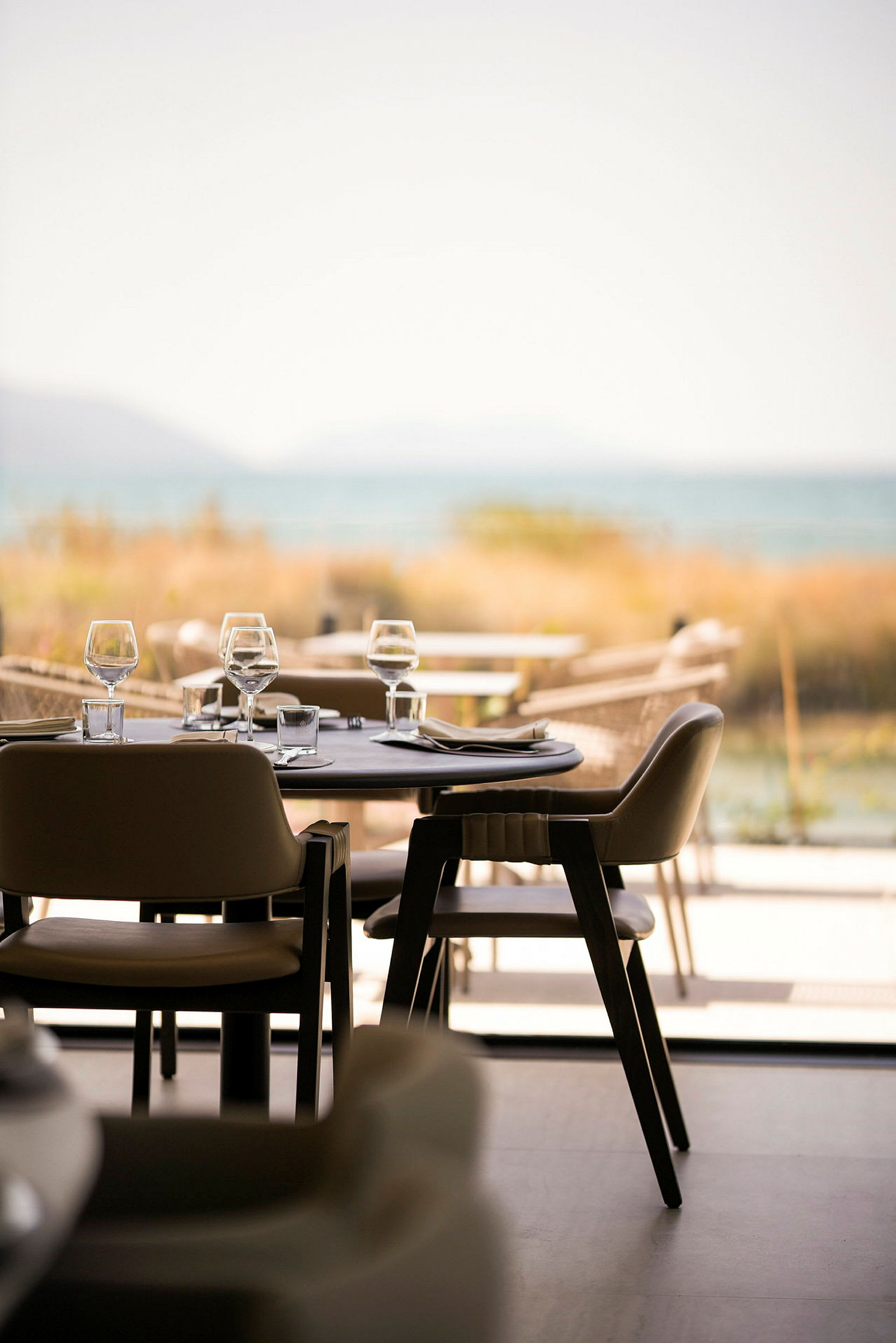 En elegant restaurant med bord og stoler dekket, med utsikt over havet. (AI-generert tekst)