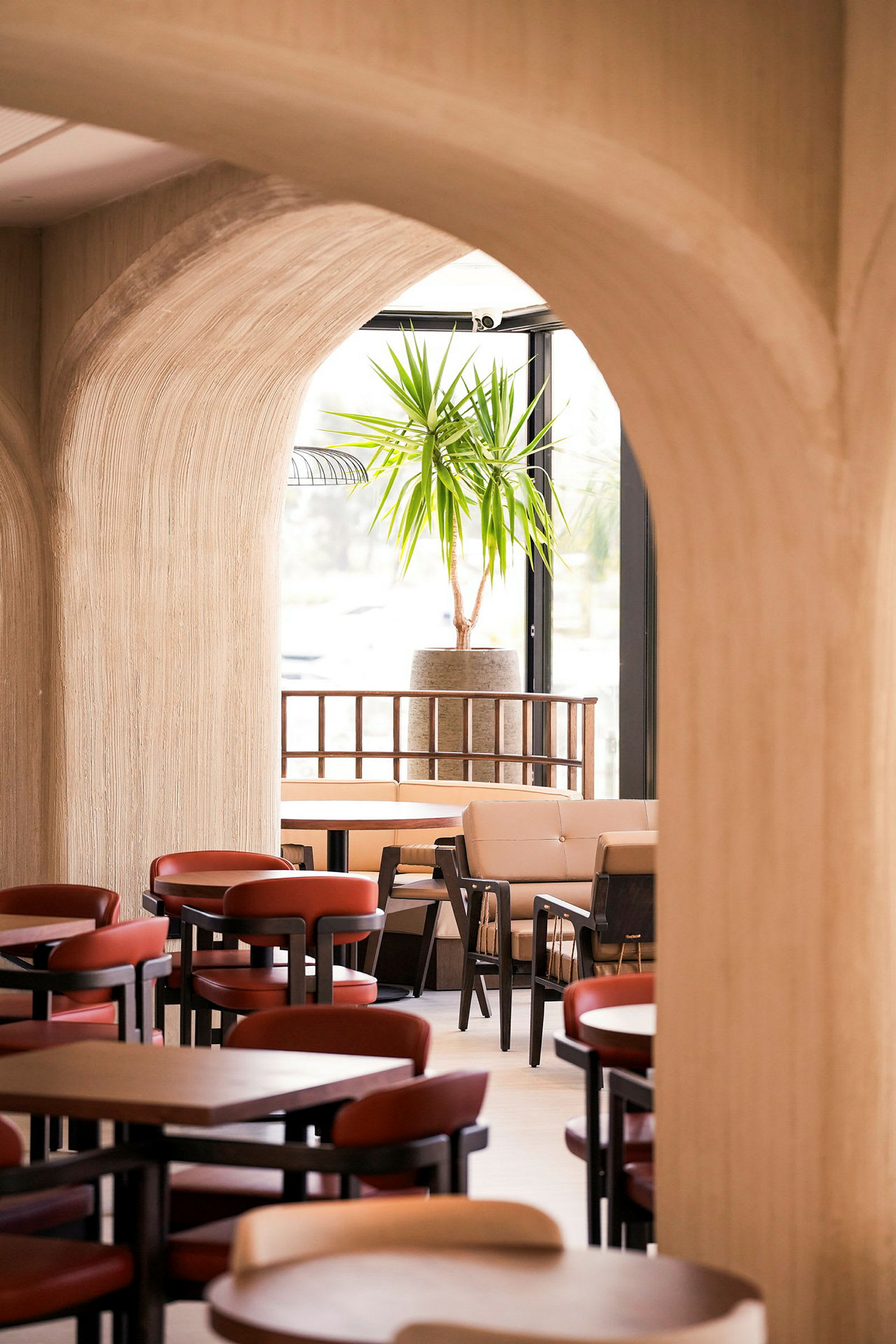 Et interiørbilde av en restaurant eller kafé med bueformede innganger, bord og stoler samt en grønn plante i bakgrunnen. (AI-generert tekst)