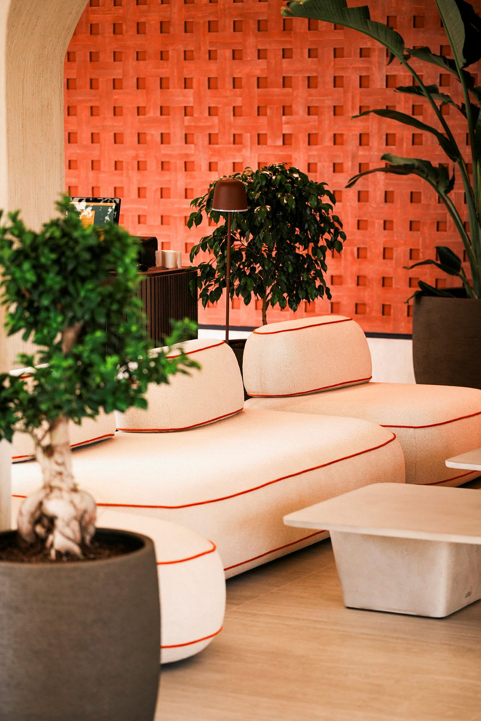 En moderne stue med en beige sofa med oransje kant, et salongbord og grønne planter foran en murvegg. (AI-generert tekst)