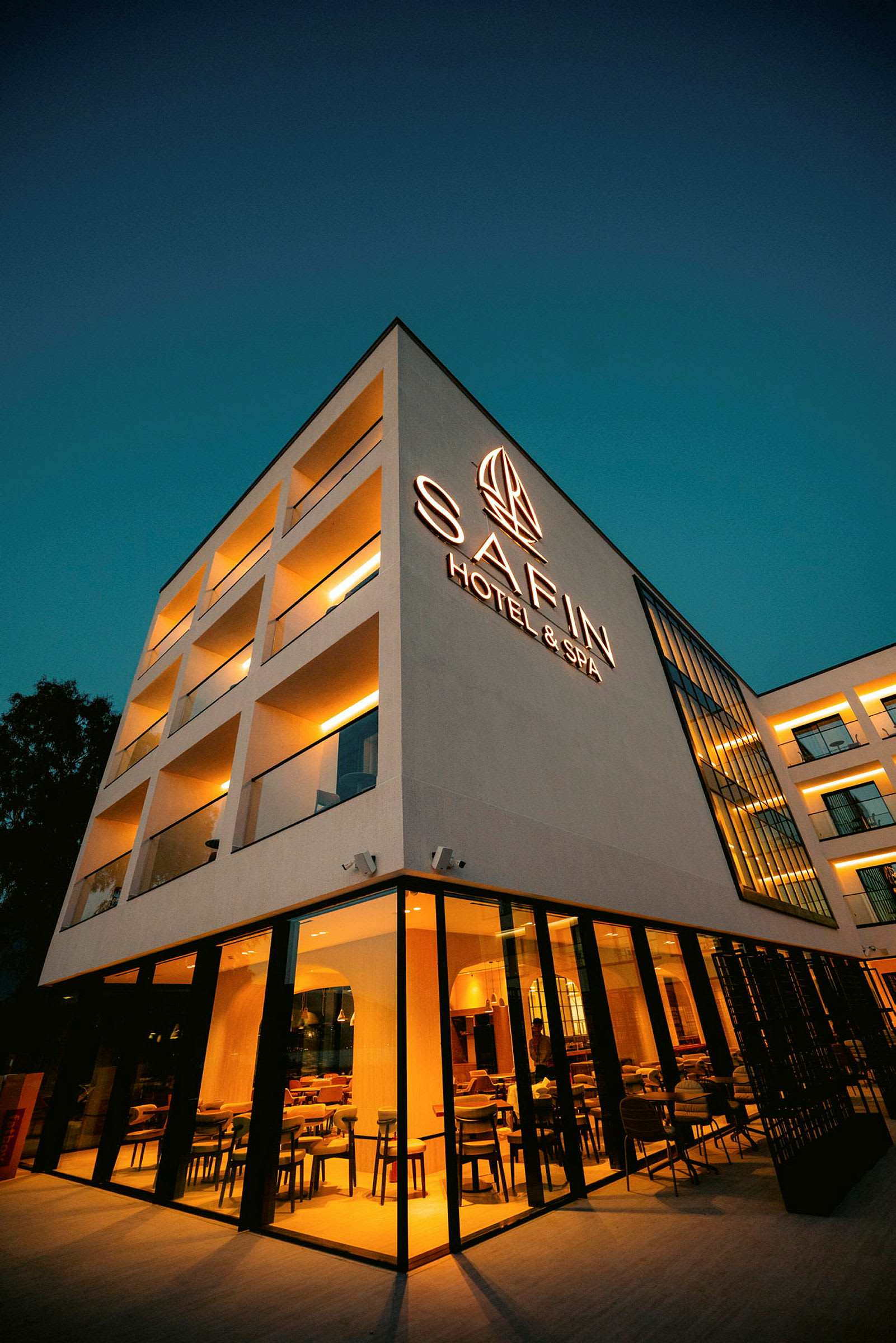 Firkantet bygning opplyst om kvelden, merket med teksten "Safin Hotel & Spa". (AI-generert tekst)