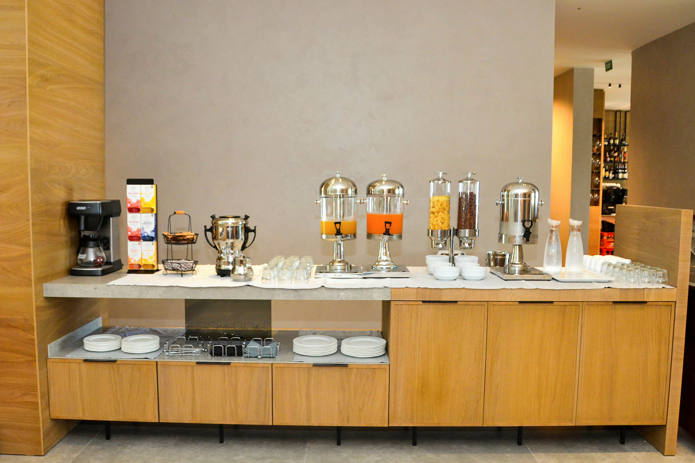 En frokostbuffet med kaffemaskin, juicebeholdere og skåler med frokostblanding på en benk. (AI-generert tekst)