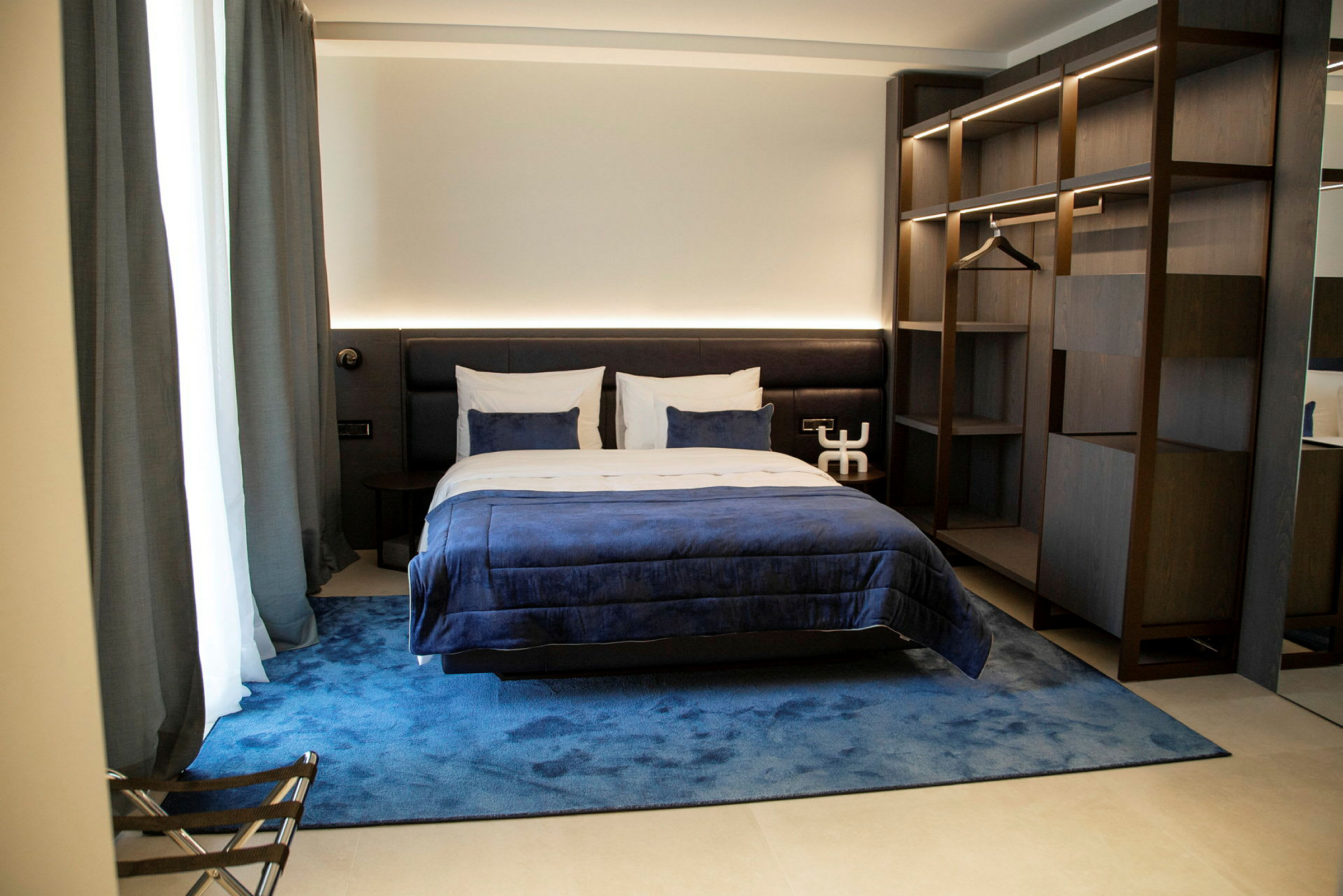 Et komfortabelt hotellrom med en dobbeltseng, blå sengetøy og en elegant innredning. (AI-generert tekst)