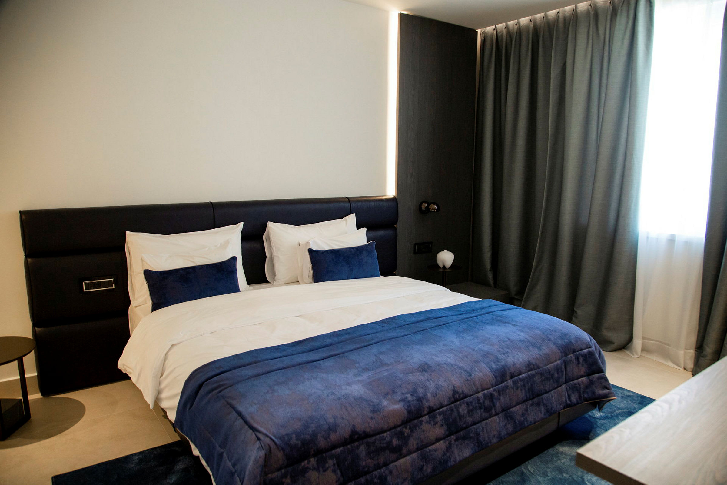 Et moderne hotellrom med en stor seng med blå sengetøy. (AI-generert tekst)