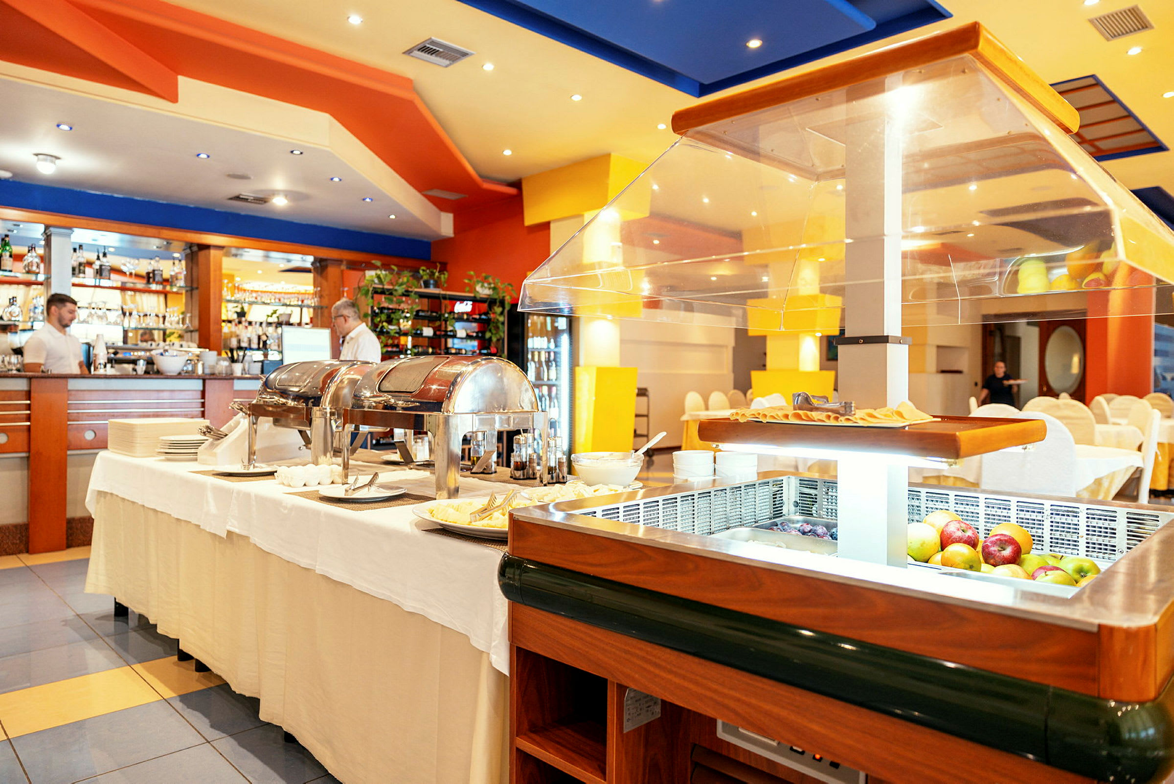 Bilde av en restaurantinteriør med buffetutstilling og glasspaneler på bordene, samt dukede bord og stoler i bakgrunnen. (AI-generert tekst)