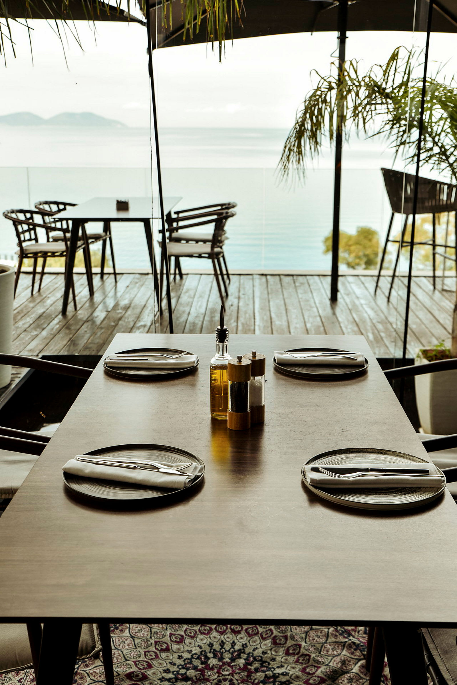 Et dekket bord med fire tallerkener og bestikk på en terrasse med utsikt over havet. (AI-generert tekst)
