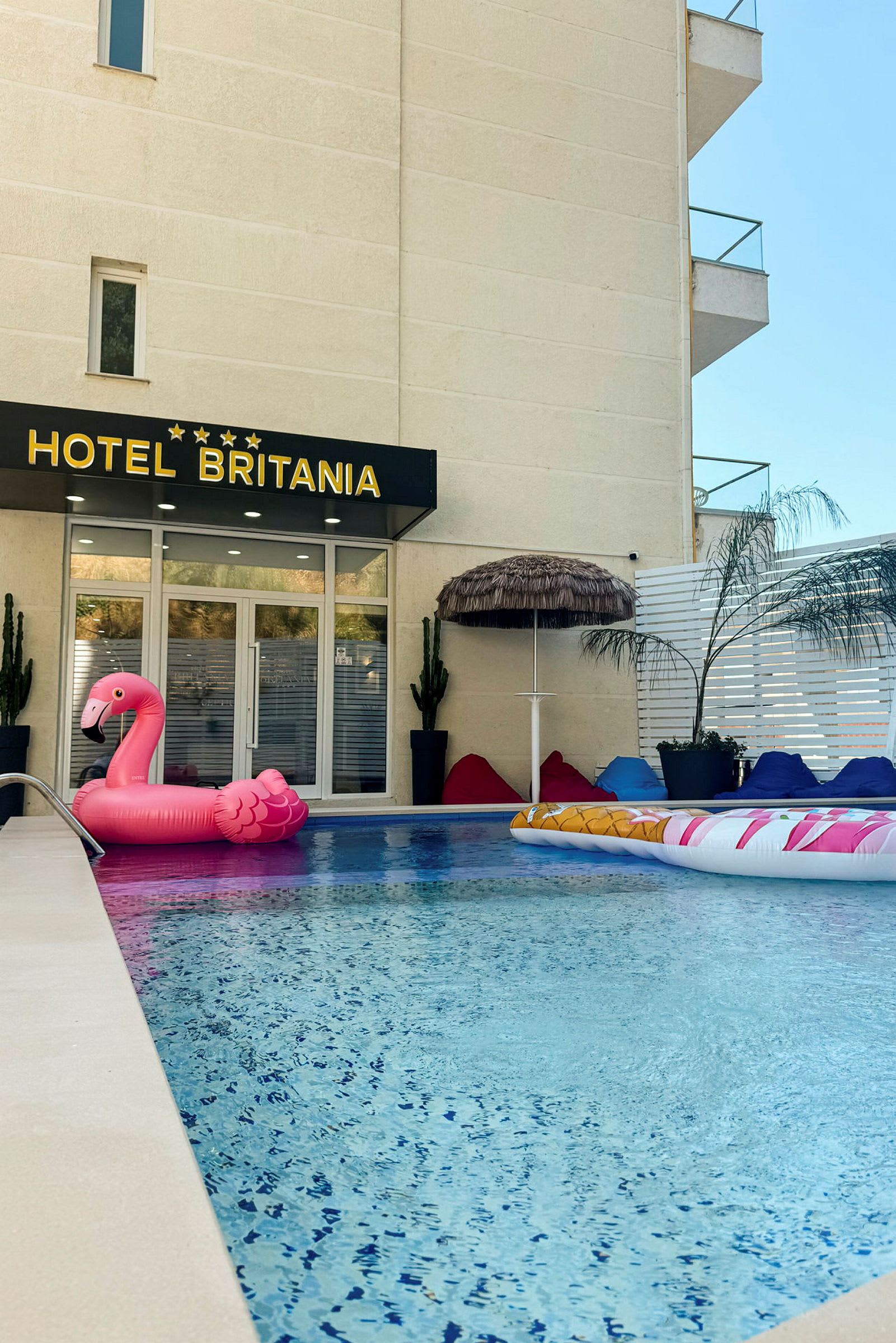 Hotellbassengområdet med en rosa oppblåsbar flamingo og sittesekker. (AI-generert tekst)