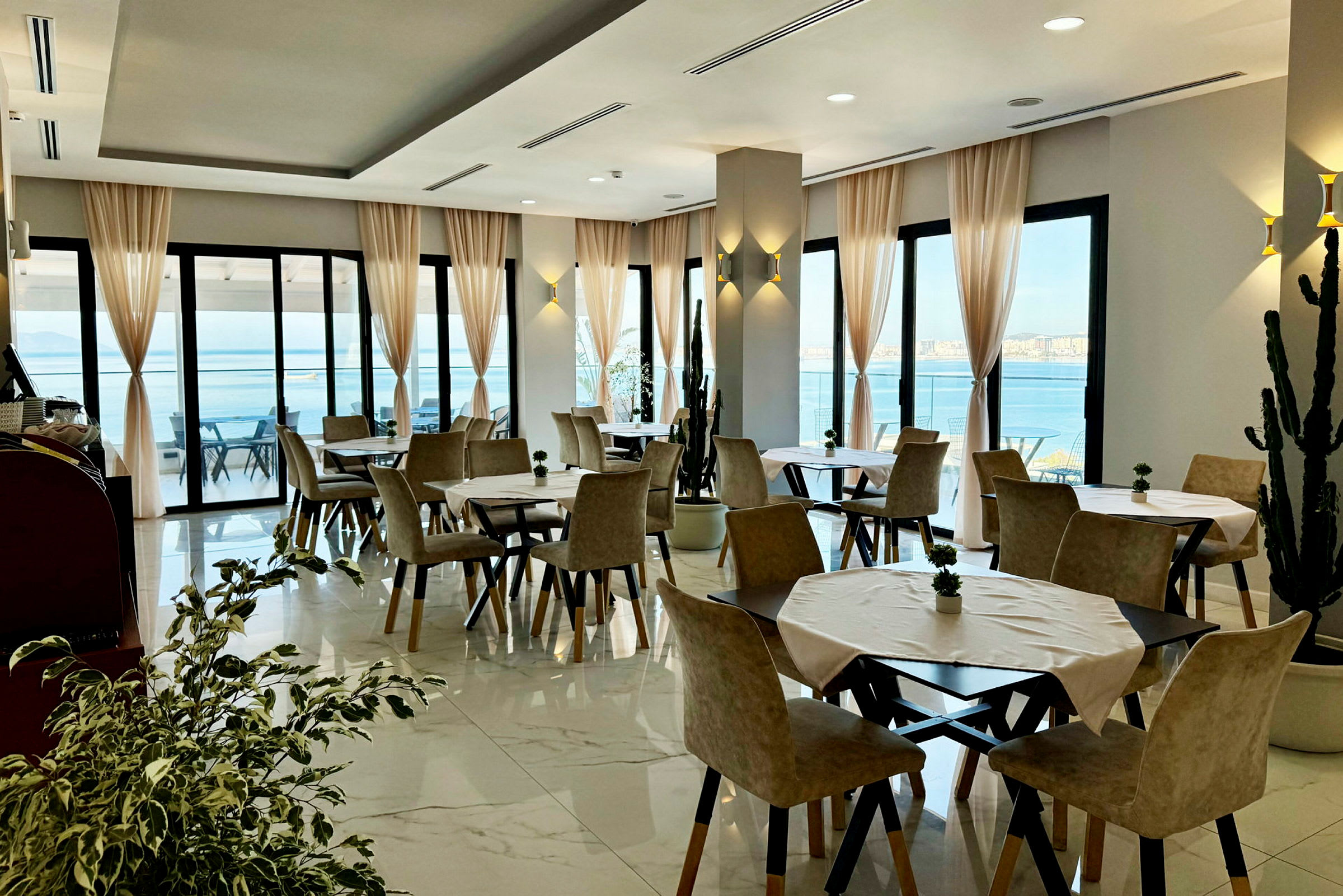 En restaurant med bord og stoler samt store vinduer med utsikt over havet. (AI-generert tekst)
