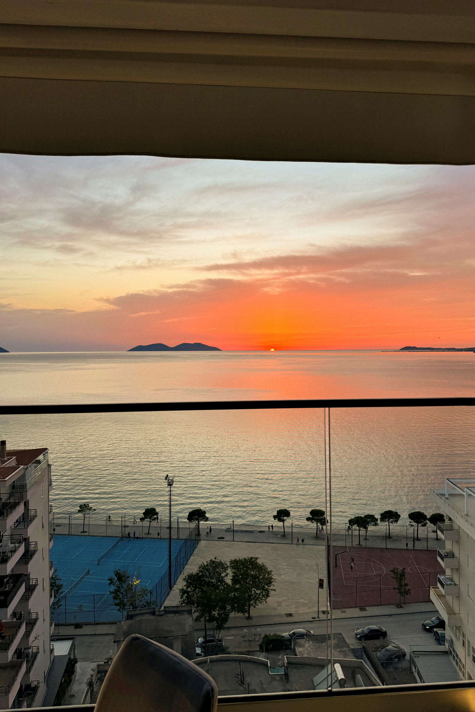 Solnedgang over havet med bygninger og idrettsplass i forgrunnen. (AI-generert tekst)