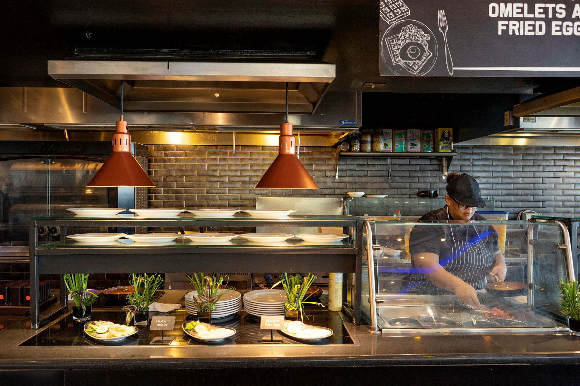 Et restaurantkjøkken med tallerkener, tilbehør og en serveringssone opplyst av varmelamper. (AI-generert tekst)