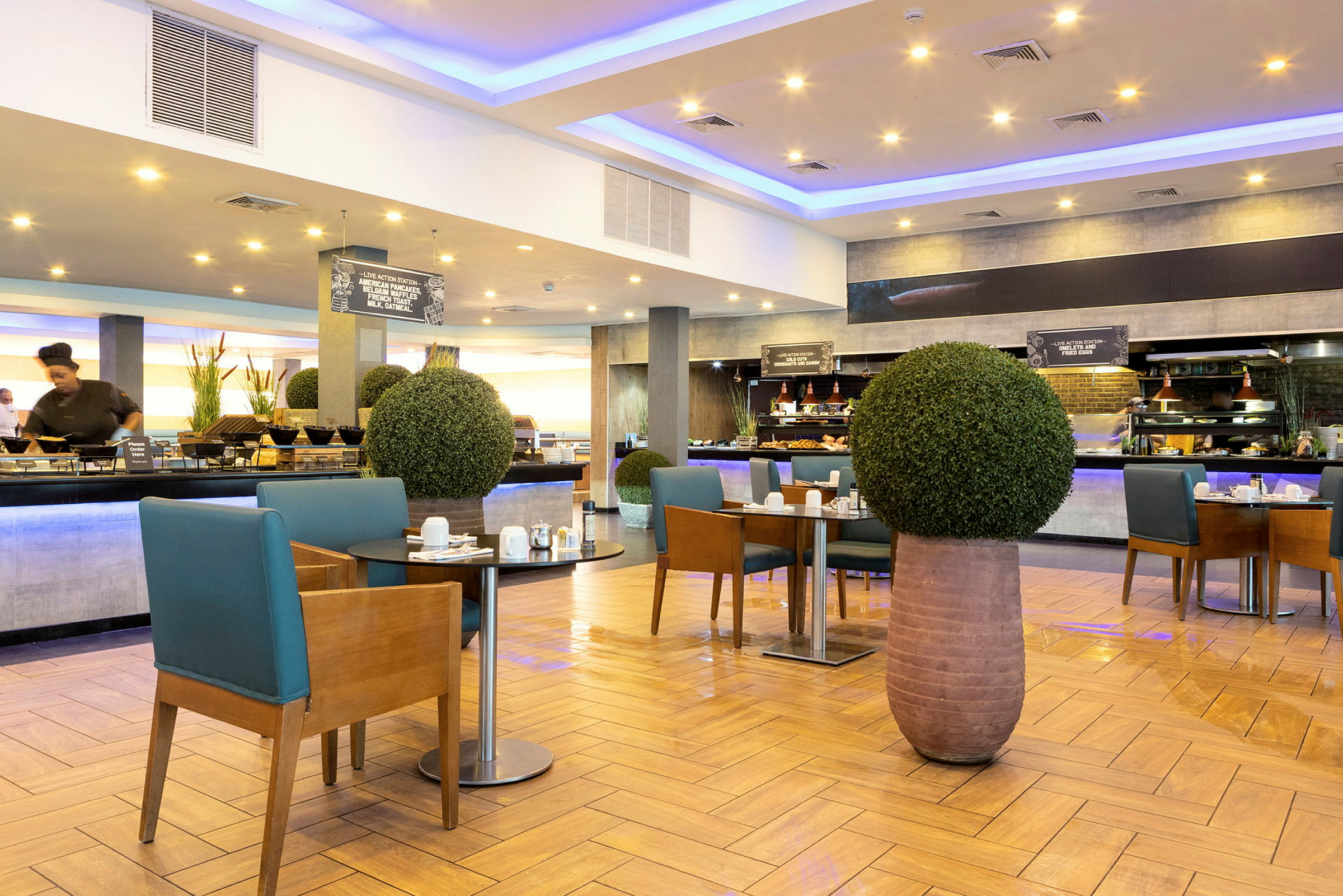En moderne hotellrestaurant med frokostbuffé og bord dekorert med grønne planter. (AI-generert tekst)