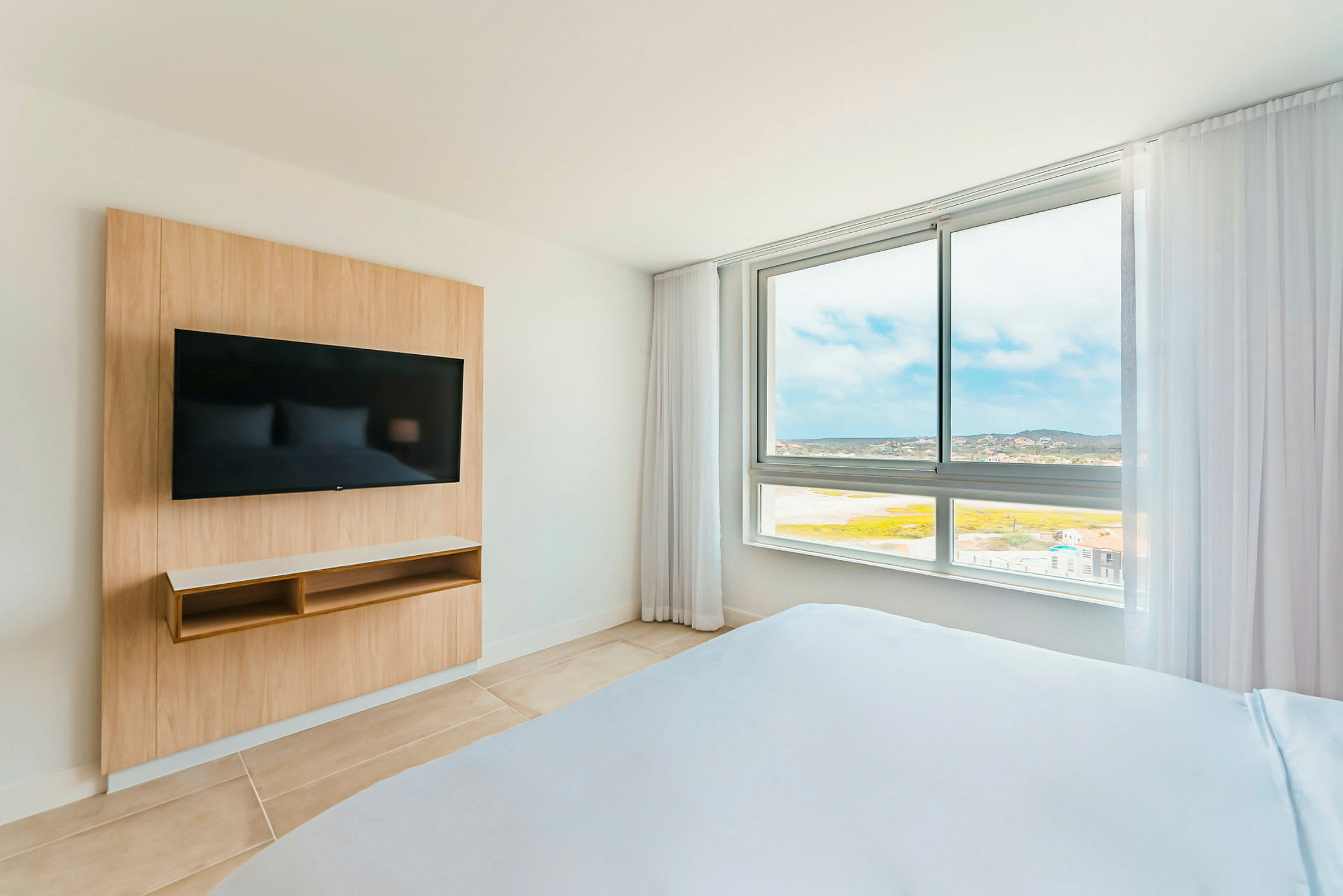 Hotellrom med en TV på veggen og utsikt gjennom et stort vindu. (AI-generert tekst)