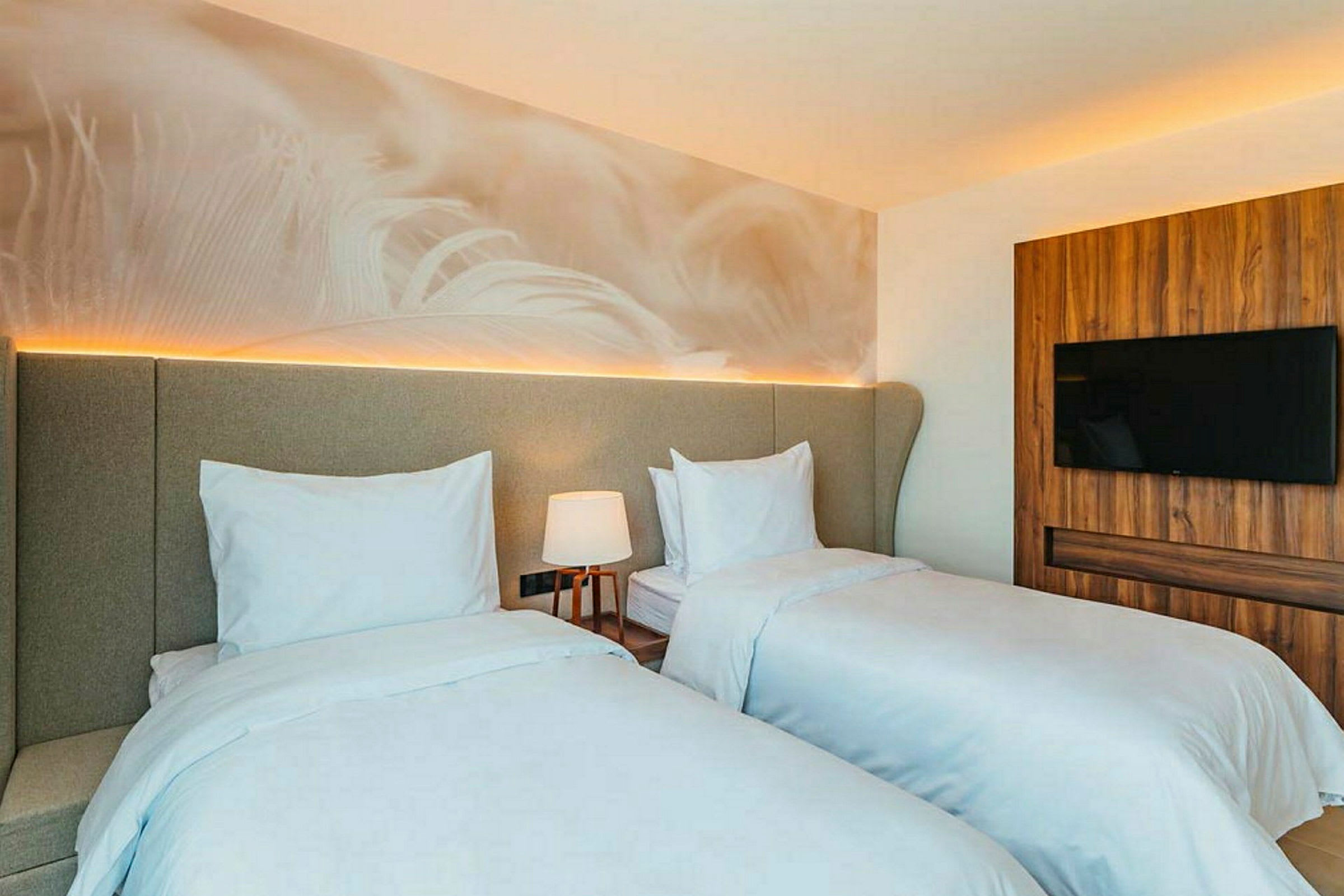 Bilde av et hotellrom med to separate senger, en lampe og en TV på veggen. (AI-generert tekst)