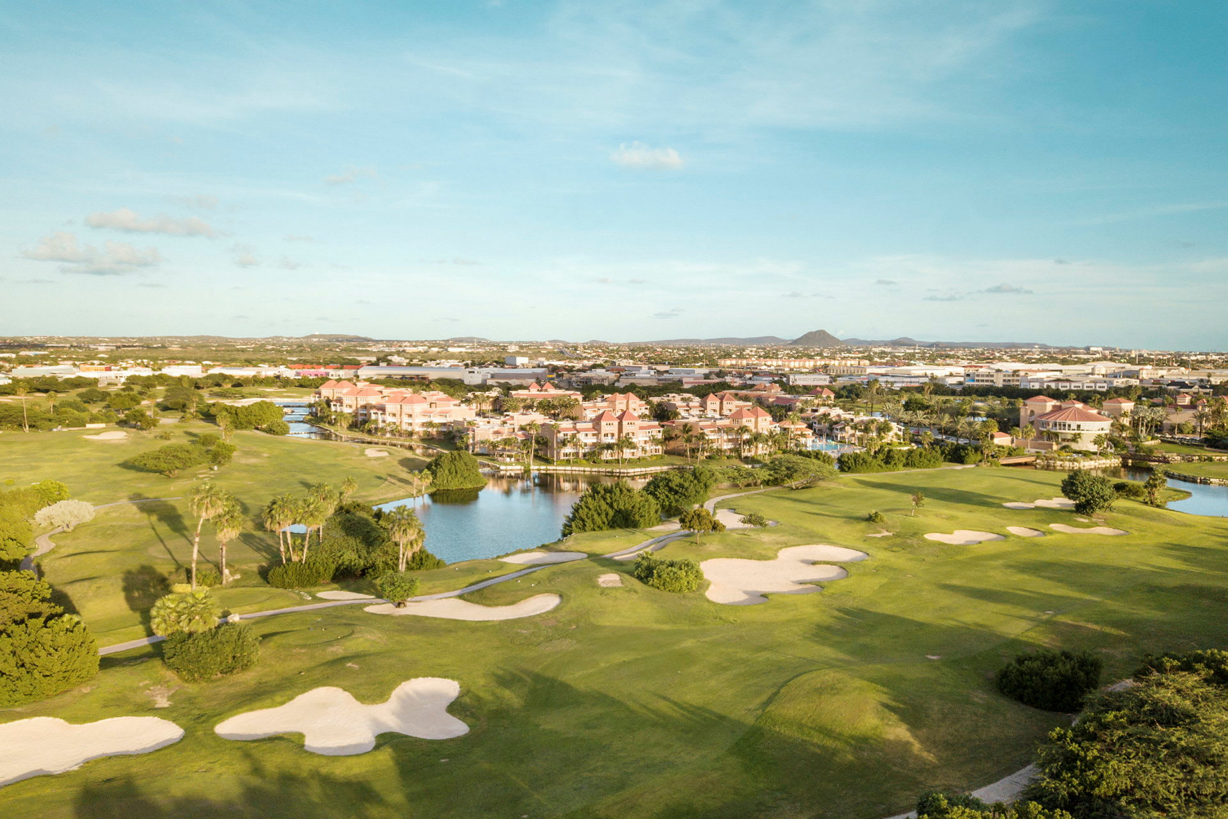 En golfbane med sandbunkere og grøntområder, ved siden av et boligområde nær vann. (AI-generert tekst)