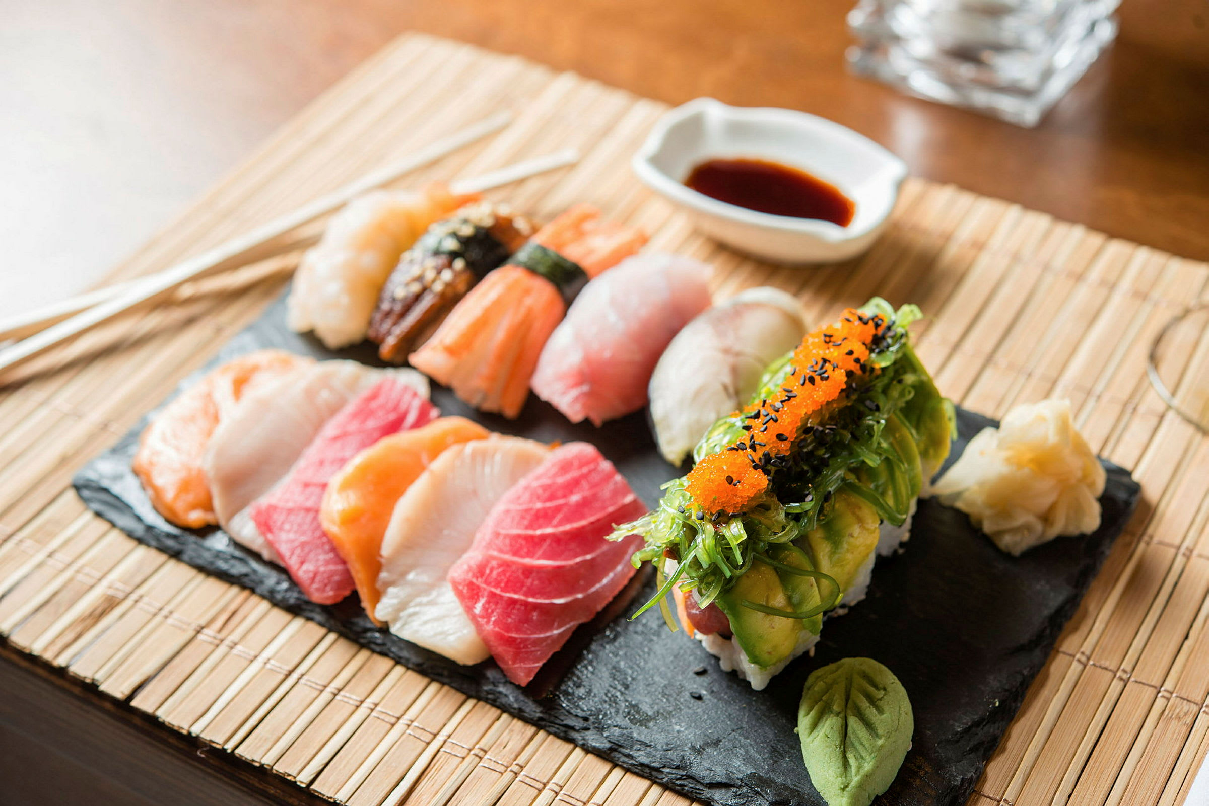 En skiferplate med forskjellige typer sushi, wasabi og syltet ingefær, samt soyasaus i en bolle. (AI-generert tekst)