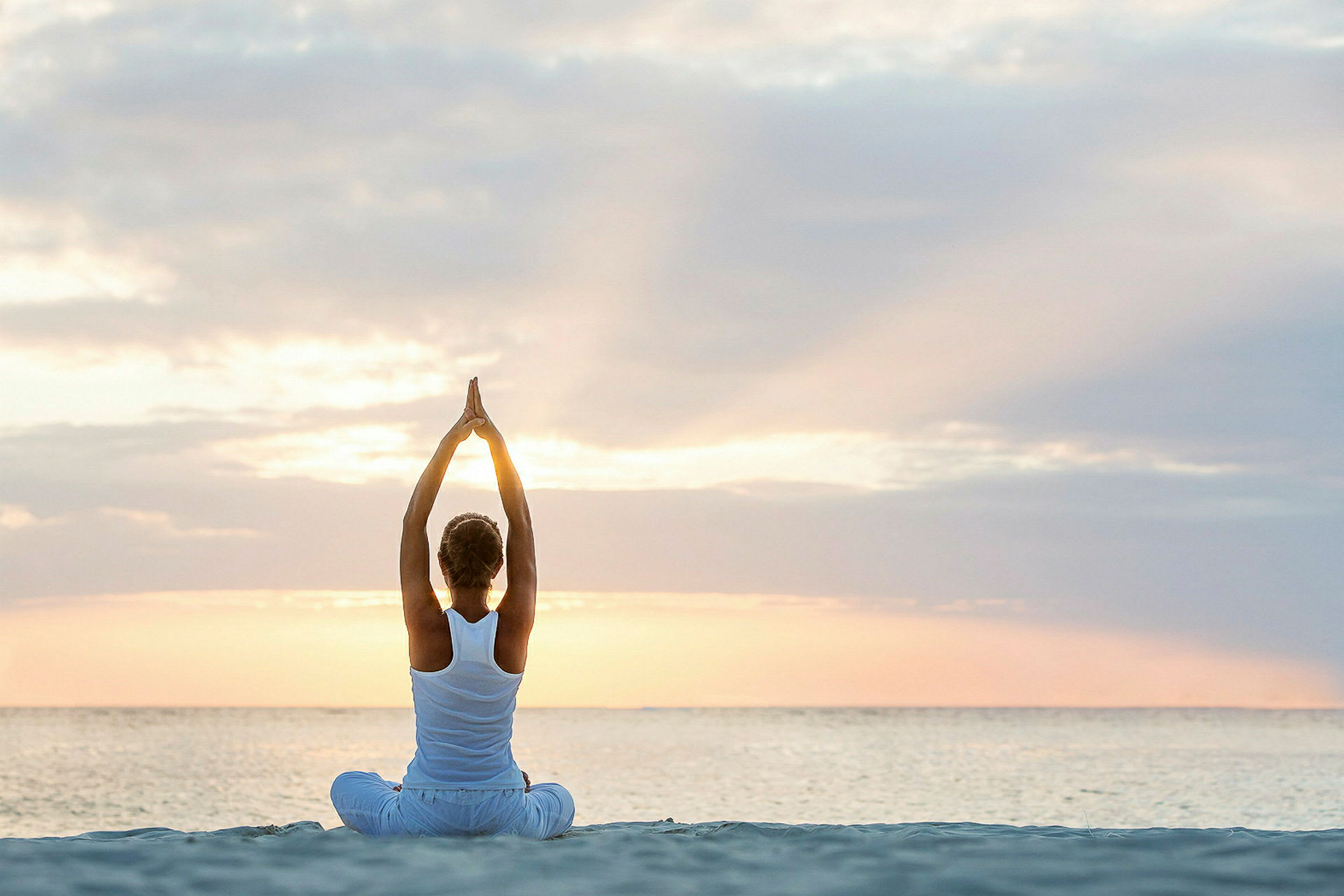 En person som sitter på stranden ved soloppgang og gjør yoga med armene oppstrakt. (AI-generert tekst)