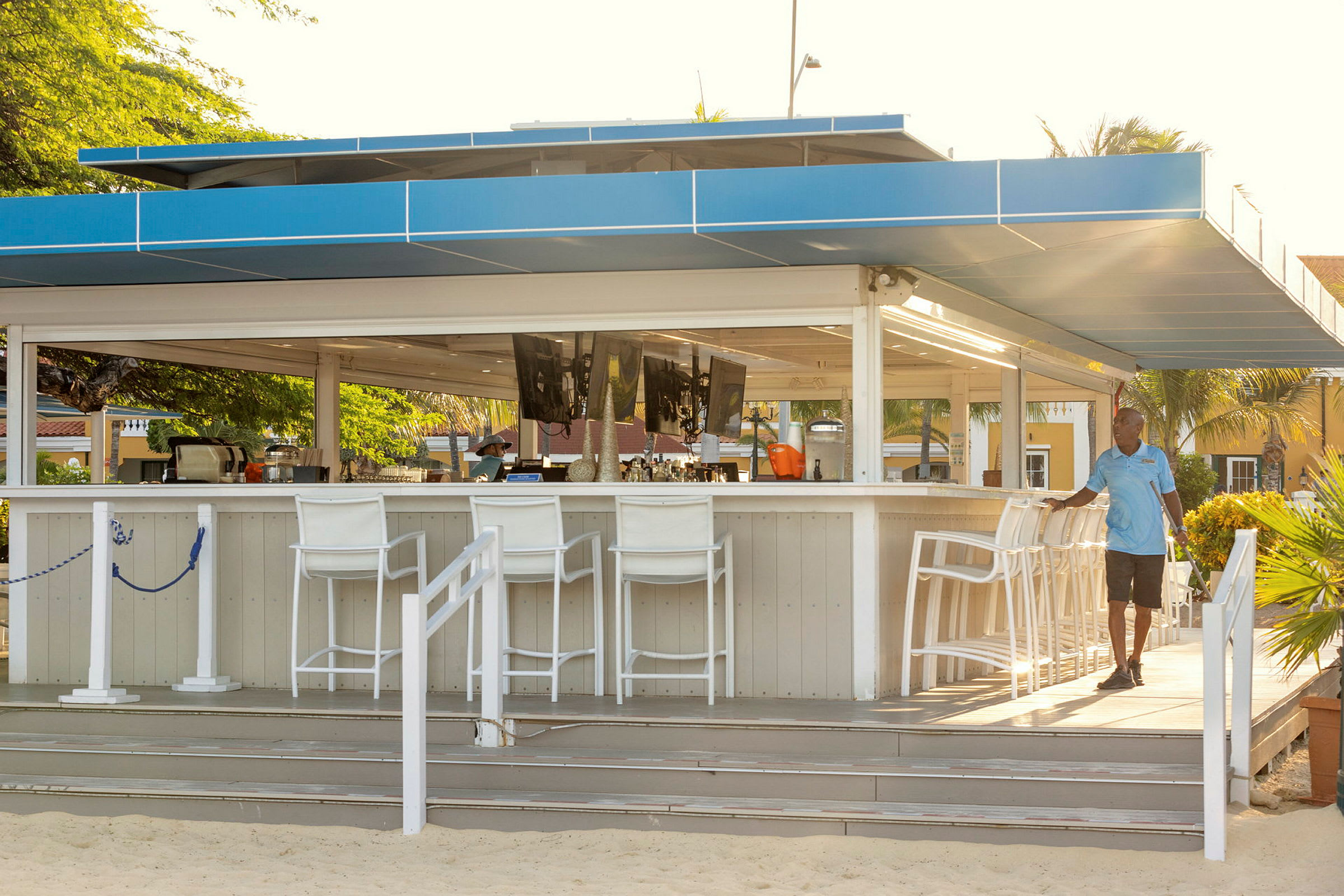 En utendørs bar med overbygg, designet i lyse farger med hvite barkrakker. (AI-generert tekst)