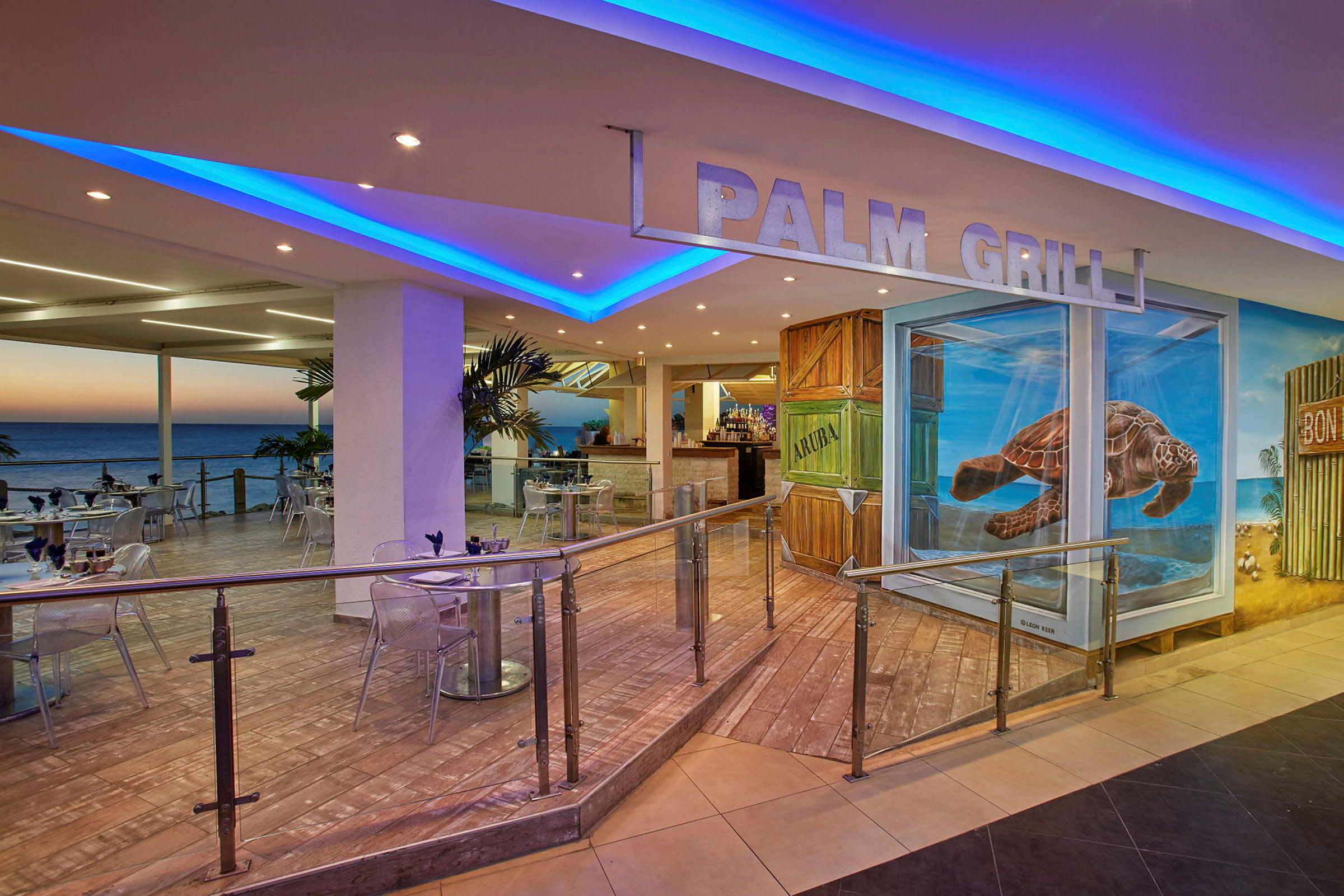 Interiøret til en restaurant med havutsikt, uteservering og et skilt med teksten "Palm Grill". Veggene er dekorert med malerier, inkludert en skilpadde. (AI-generert tekst)