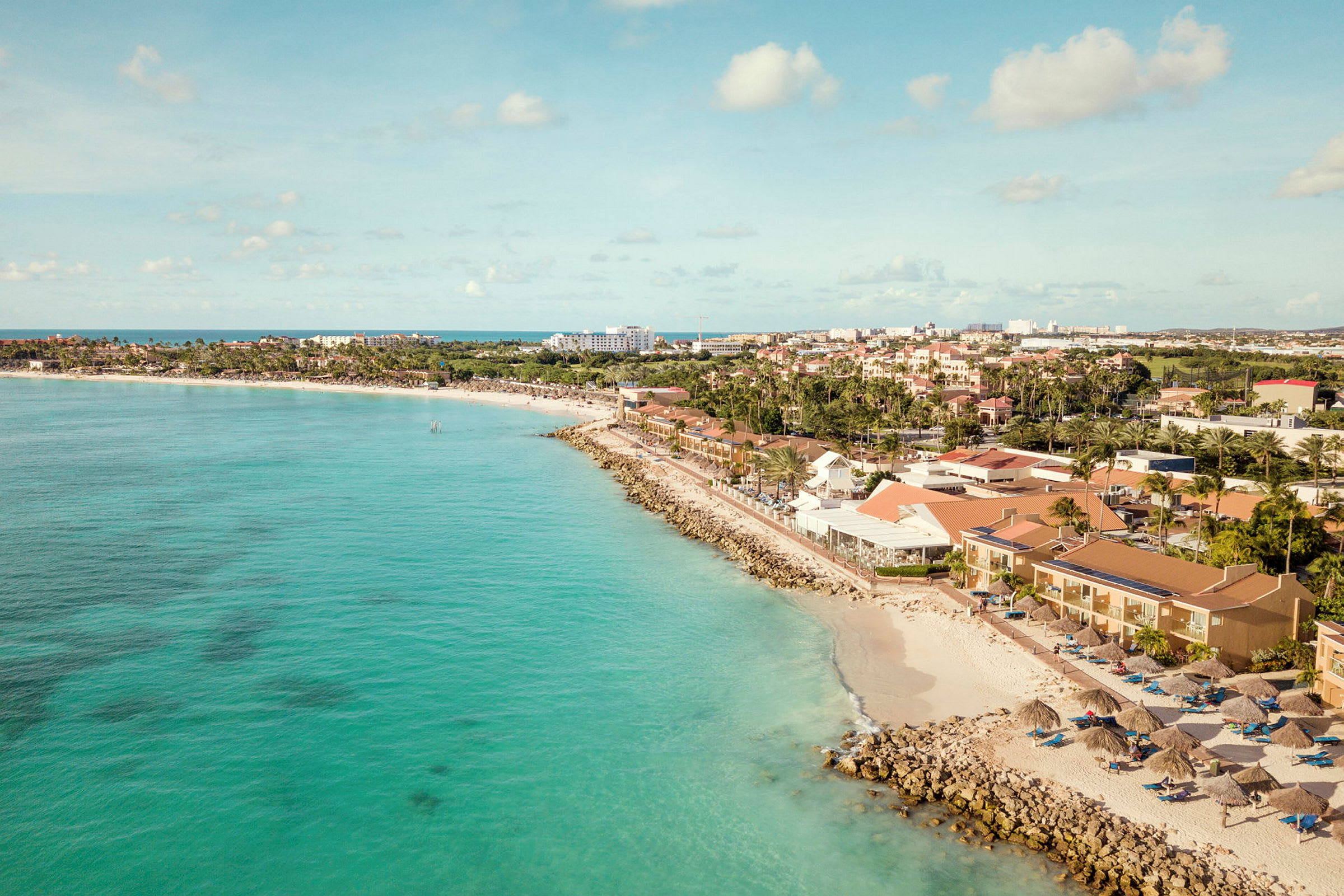Strand med turkist vann, omkringliggende bygninger og solparasoller. (AI-generert tekst)