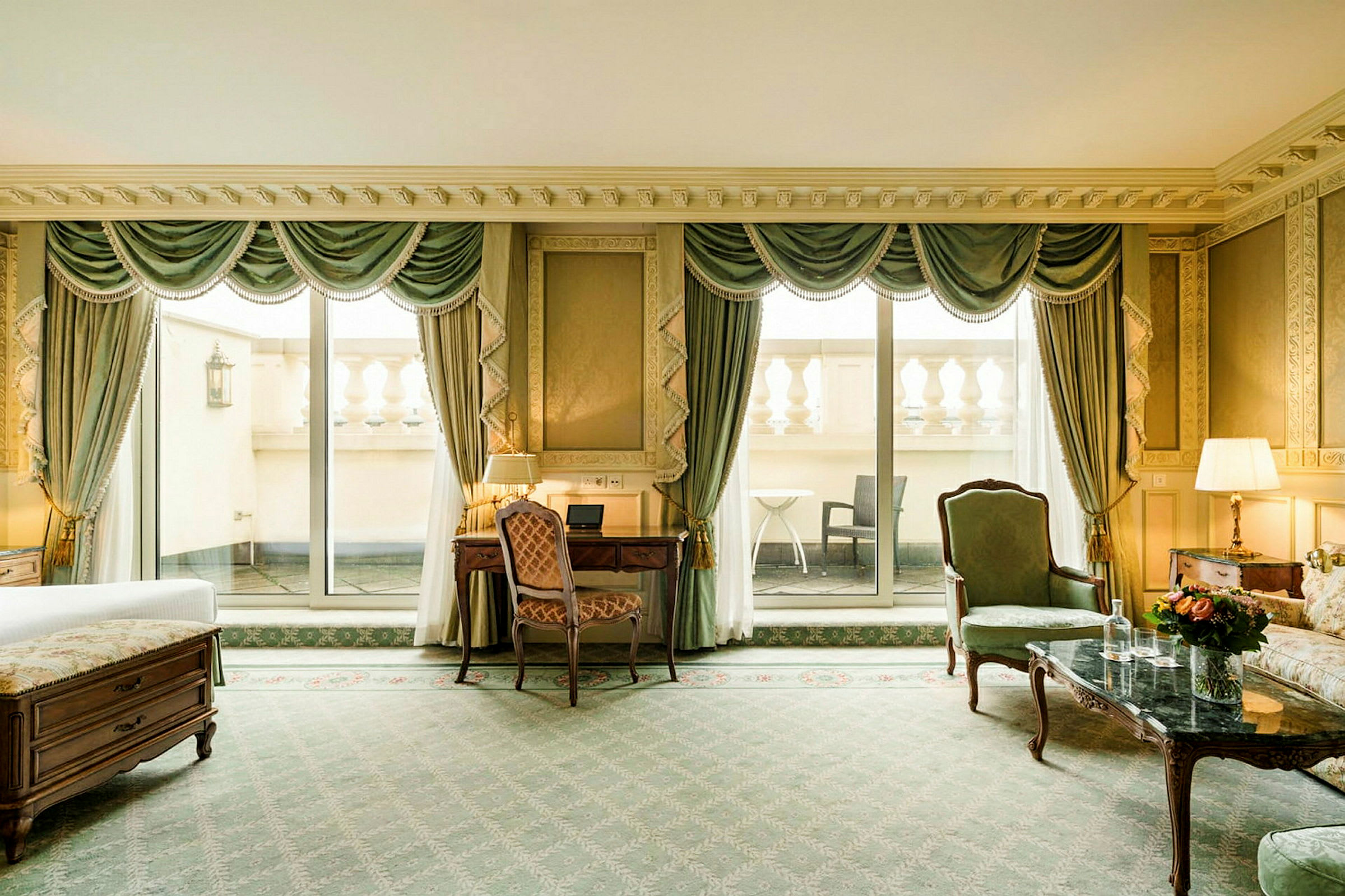 Et elegant stue med klassiske møbler, høye gardiner, en sofa og et skrivebord. Store vinduer med utsikt over en terrasse. (AI-generert tekst)