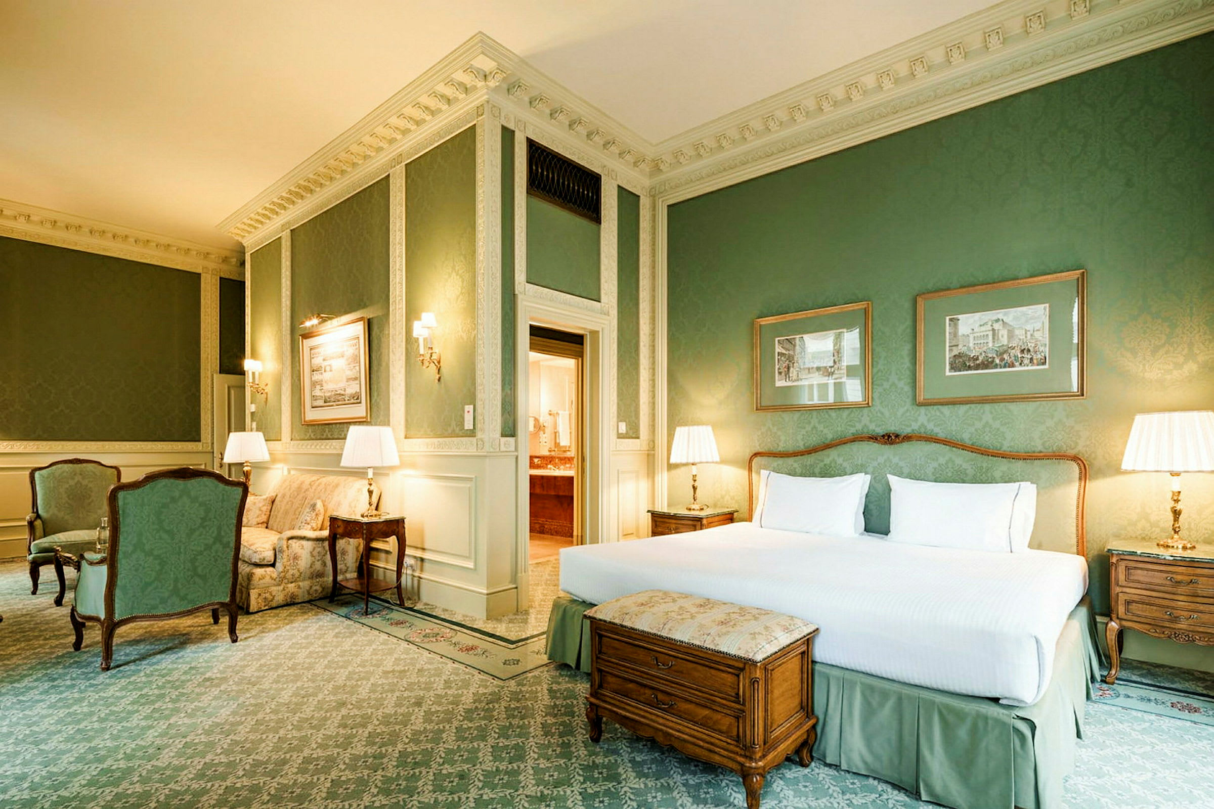 Et elegant hotellrom med en stor dobbeltseng, to nattbord med lamper, en sittegruppe og grønne veggbekledninger. (AI-generert tekst)