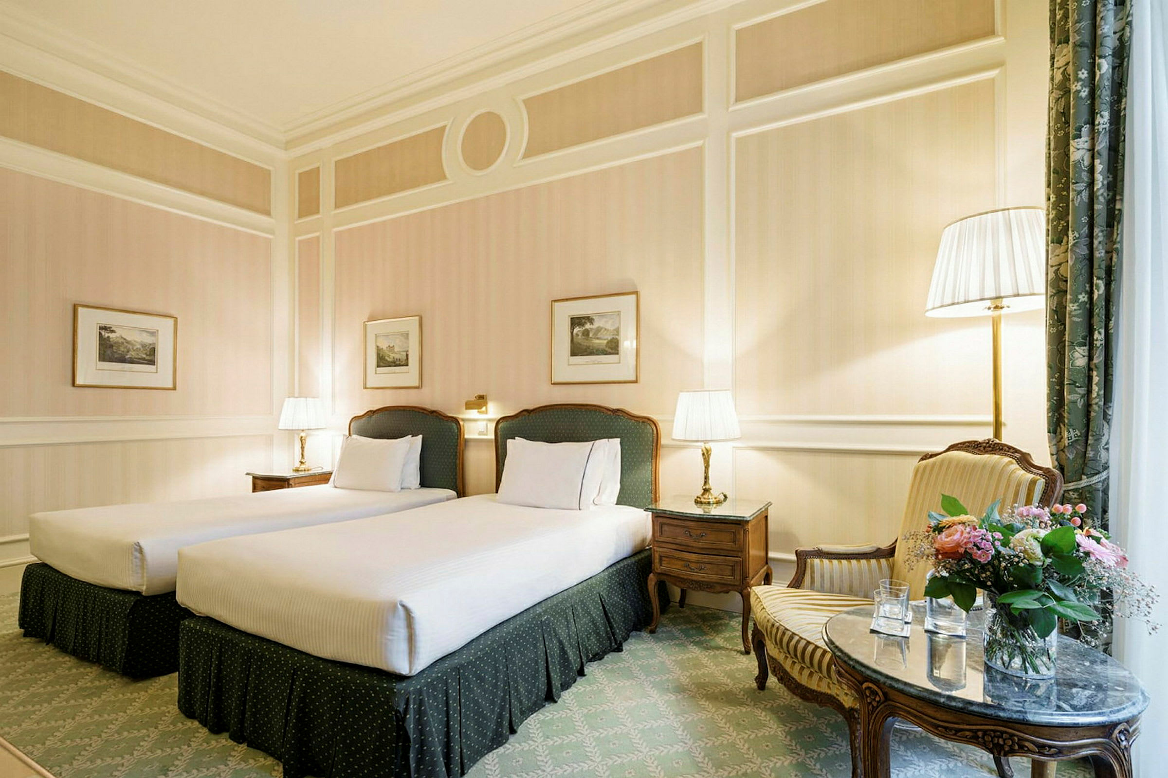 Velmøblert hotellrom med to enkeltsenger, nattbord med lamper, lenestol, bord med blomsterkrukke og dekorerte vegger. (AI-generert tekst)