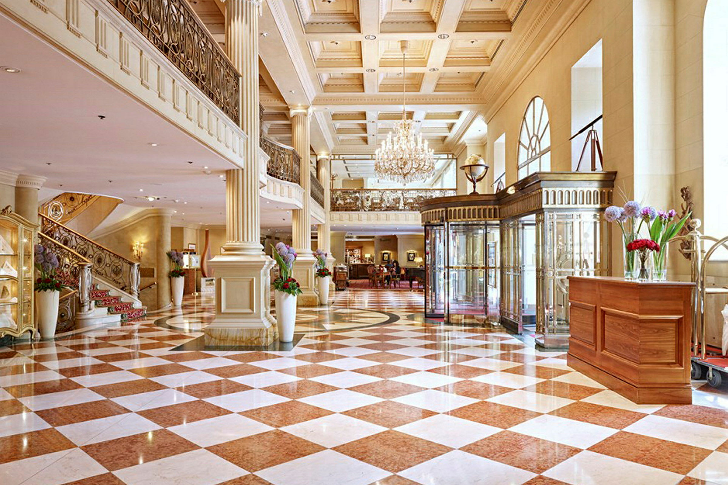 En luksuriøs hotellobby med marmorfliser, søyler, en lysekrone og en elegant trapp. (AI-generert tekst)