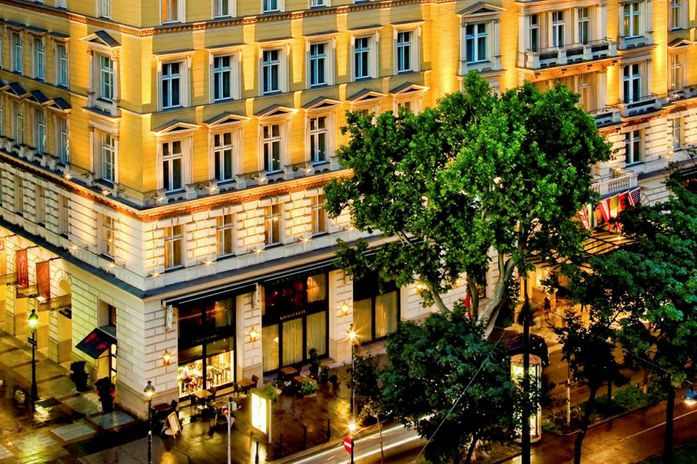 Et opplyst hotell med flere etasjer, store vinduer og vegetasjon foran bygningen. (AI-generert tekst)