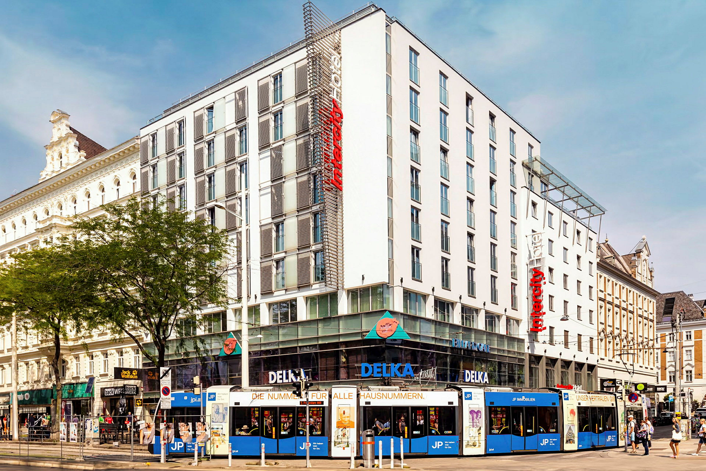 En flerfarget trikk foran et moderne hotell i bymiljø. (AI-generert tekst)