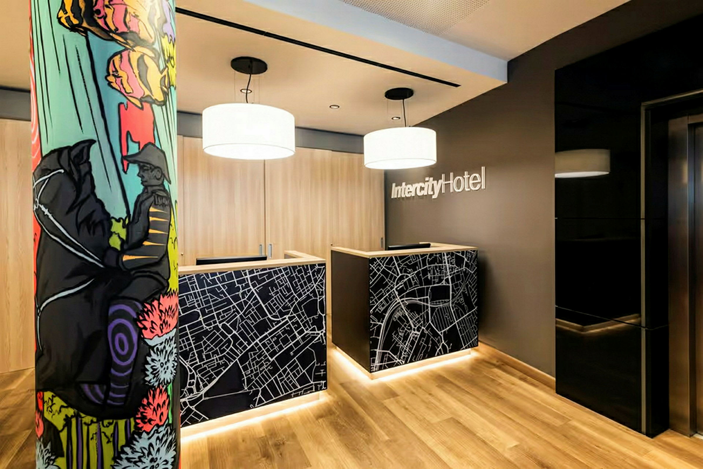 Resepsjonen med to skranker dekorert med kartmotiv i lobbyen på IntercityHotel. En fargerik søyle vises til venstre. (AI-generert tekst)