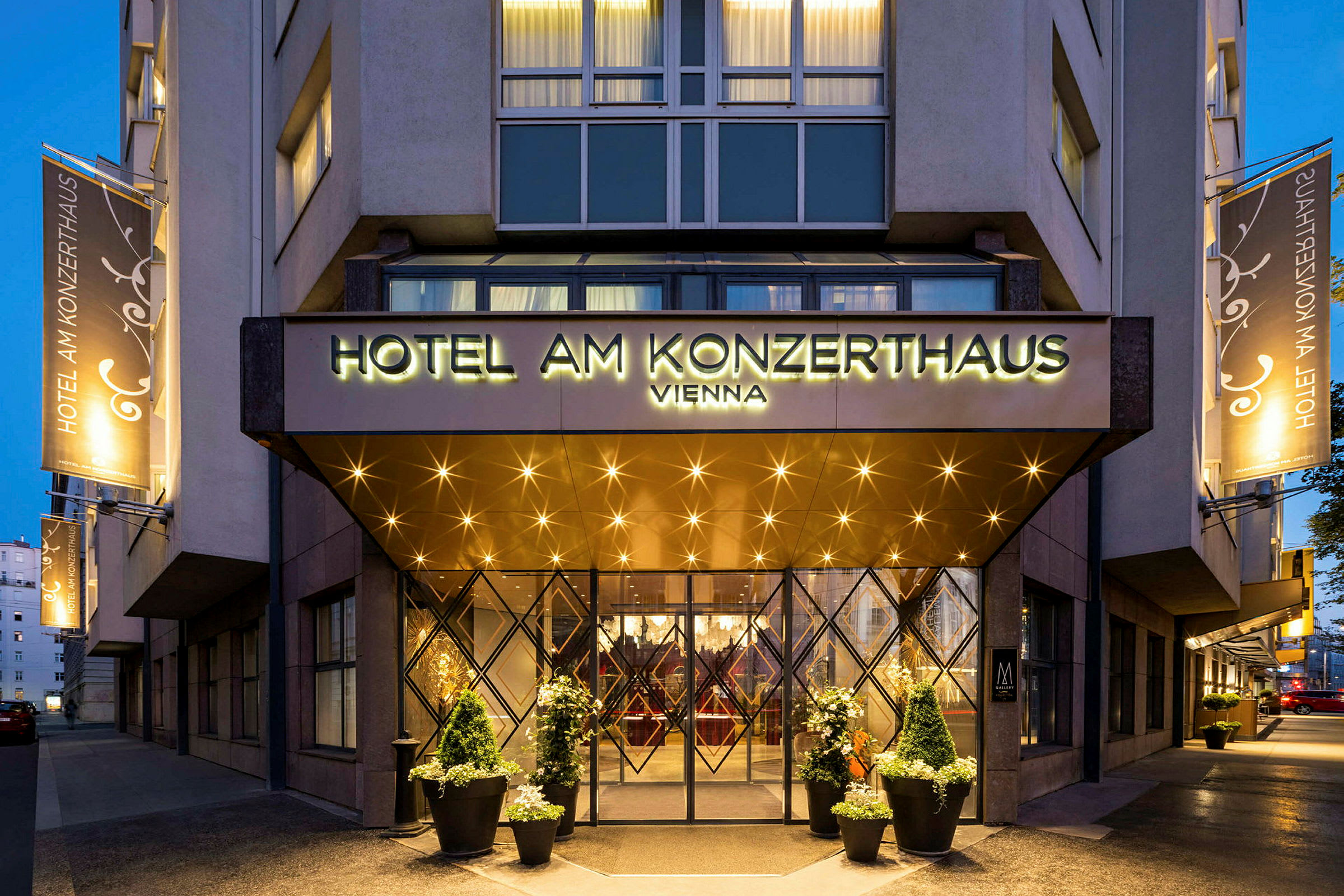 Inngangen til et hotell med et skilt som lyder "Hotel am Konzerthaus Vienna". Belysning og dekorasjoner er synlige rundt inngangen og på fasaden. (AI-generert tekst)
