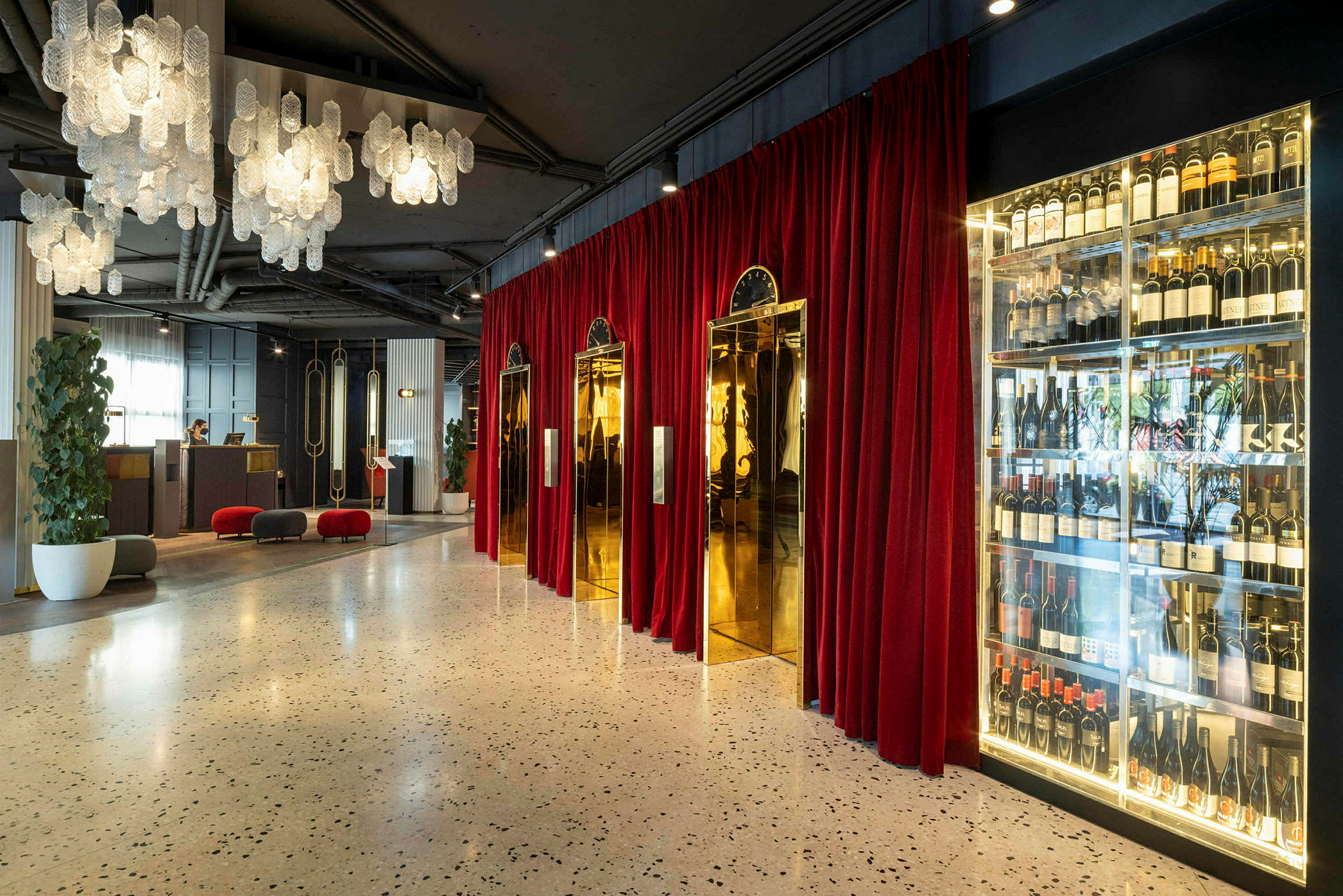 Hotellobby med hengende lysekroner, røde gardiner, gyldne heisdører og en vinoppbevaring. (AI-generert tekst)