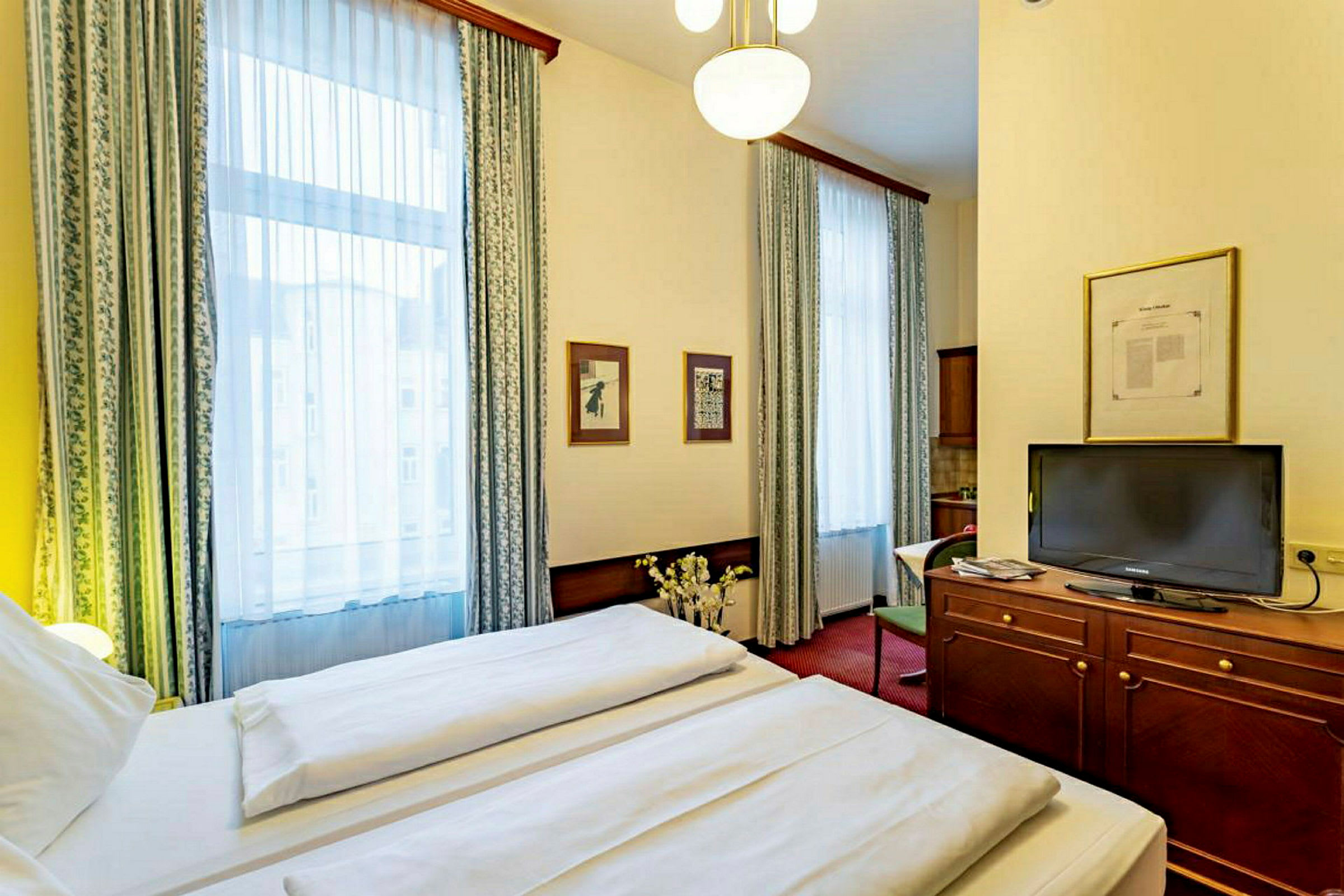 Interiør av et hotellrom med en dobbeltseng, en TV på en trekommode og to store vinduer med gardiner. (AI-generert tekst)