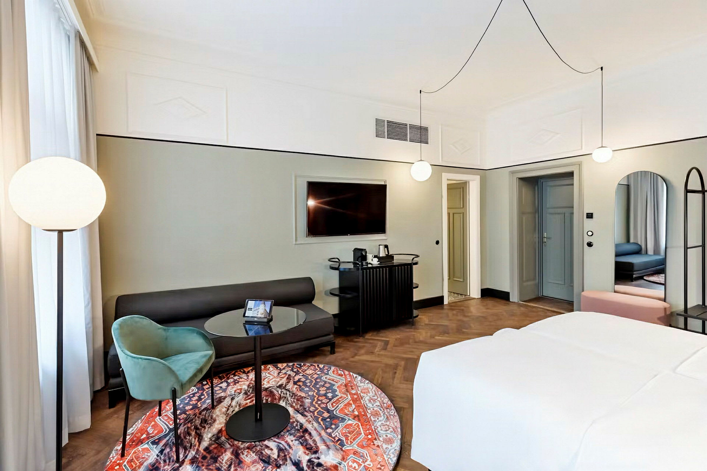 Et moderne hotellrom med en komfortabel seng, en sofa, et lite rundt bord med en lenestol og en stor TV på veggen. (AI-generert tekst)