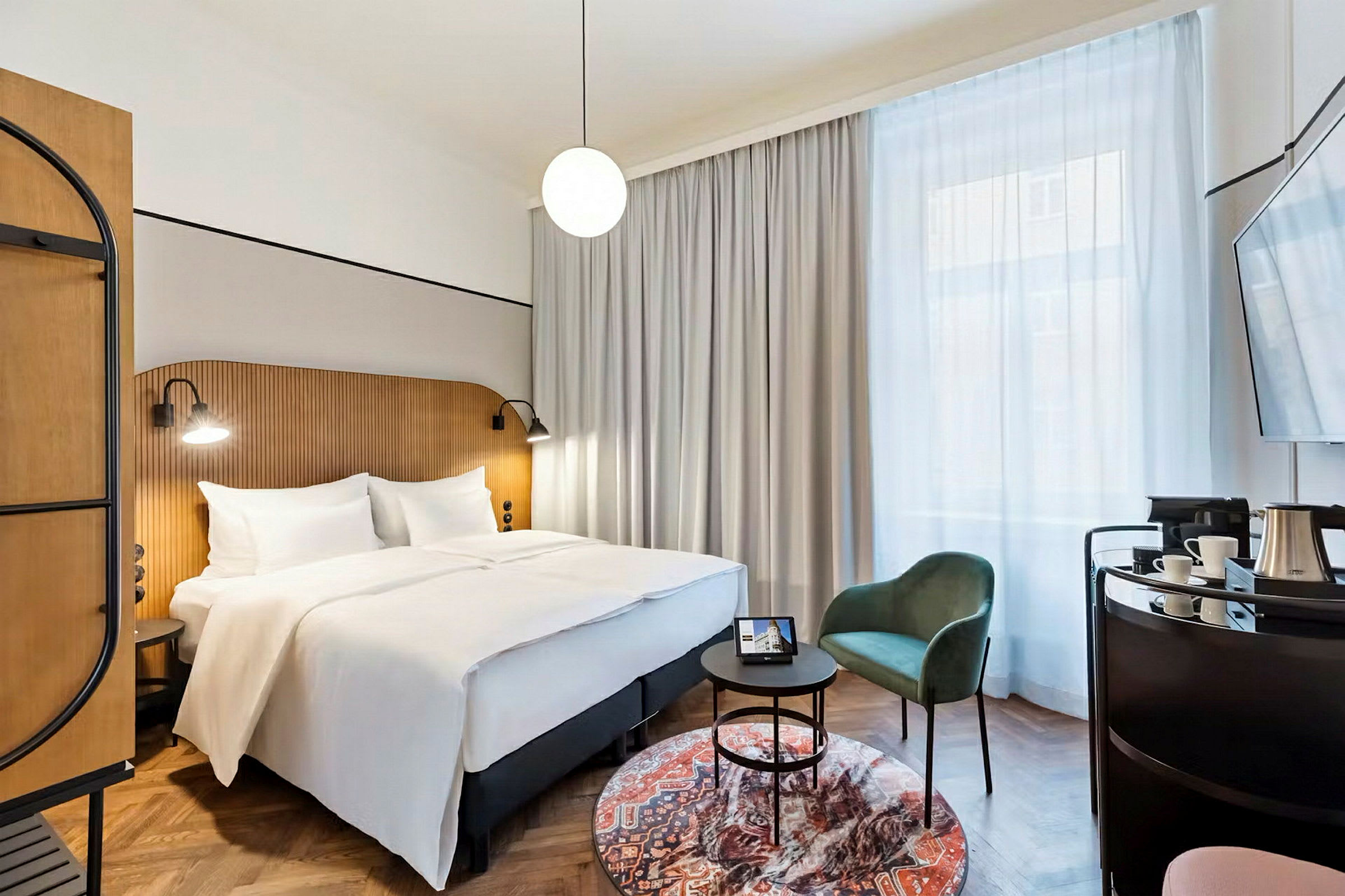 Et hotellrom med en dobbeltseng, en stol og et bord samt et stort vindu med gardiner. (AI-generert tekst)