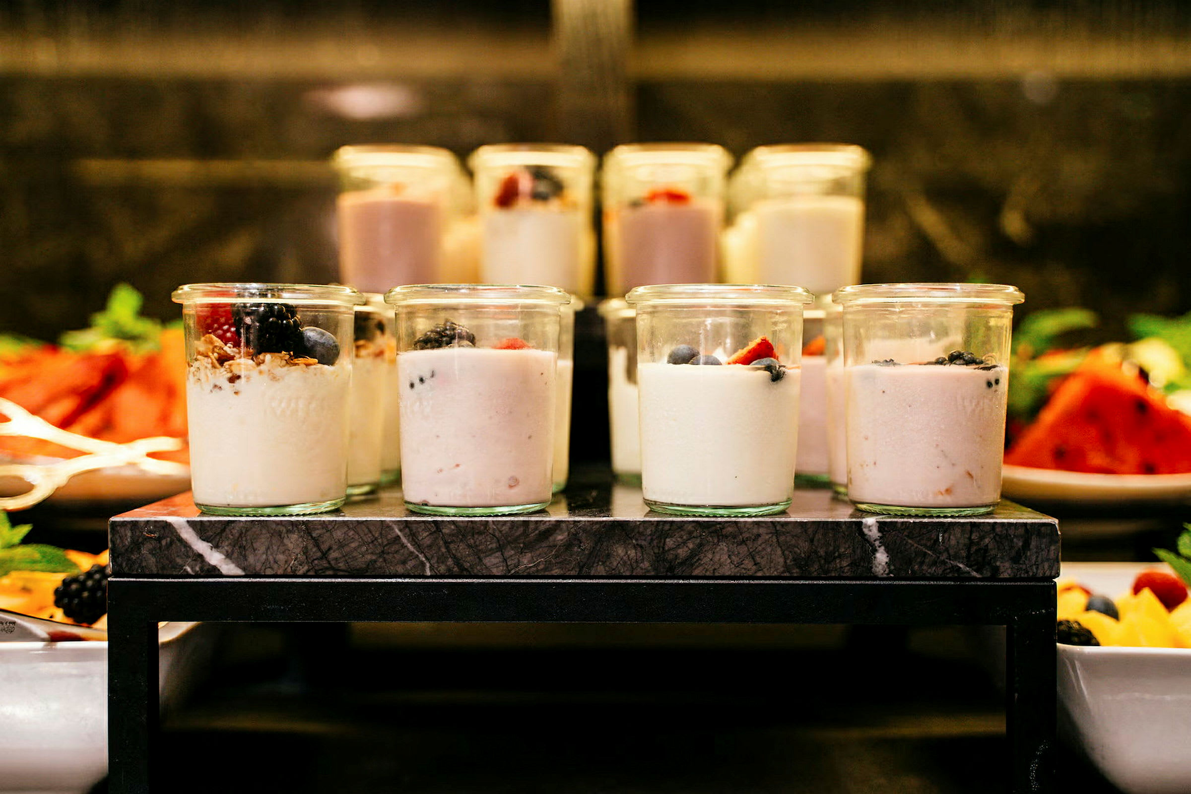 Flere små glasskrukker fylt med yoghurt og toppet med bær og granola. (AI-generert tekst)