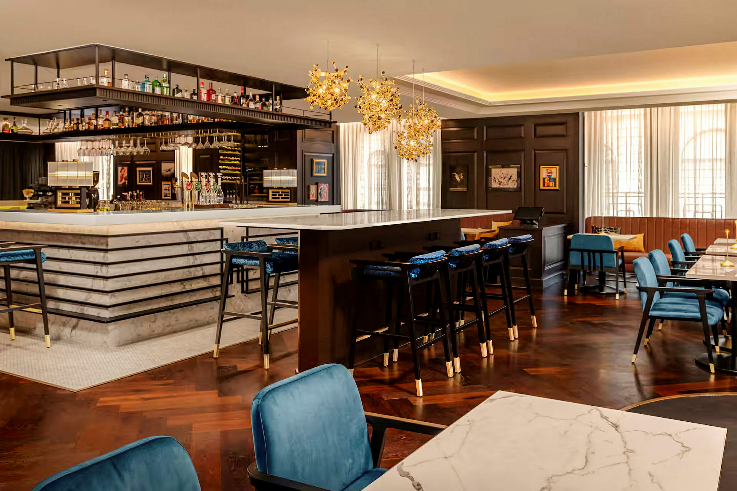 En elegant bar med marmordisk og hengende lamper over, sitteplasser og bord i den omkringliggende spisestuen. (AI-generert tekst)