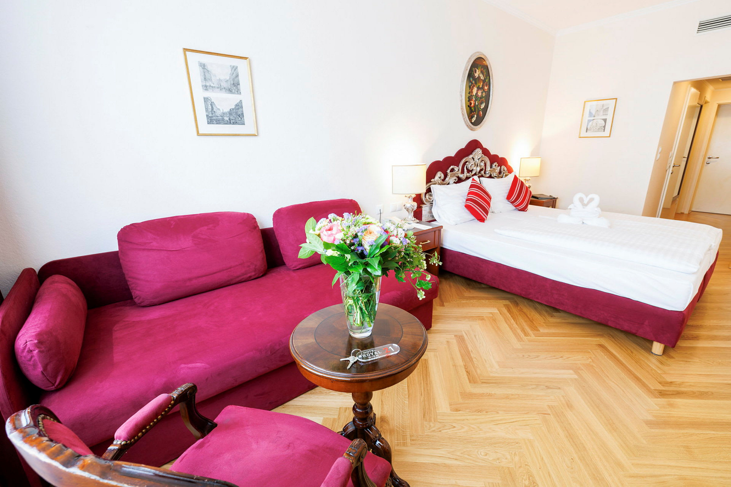 Et hotellrom med en rød sofa, et rundt bord med en blomsterbukett og en seng med røde detaljer. (AI-generert tekst)