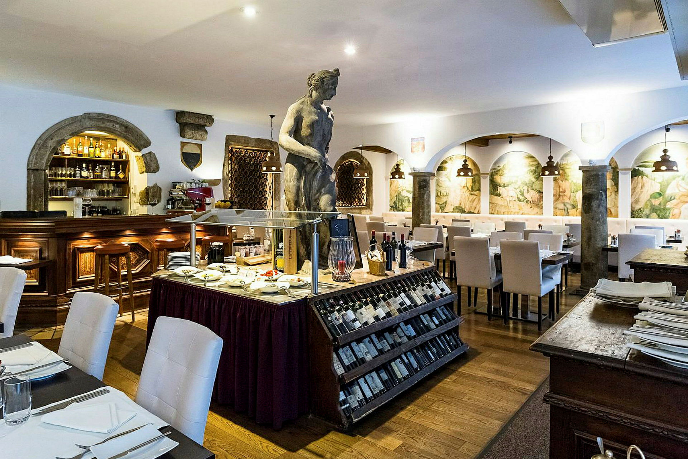 En restaurant med hvit innredning, en skulptur i midten, og en utstilling med vin og delikatesser. (AI-generert tekst)