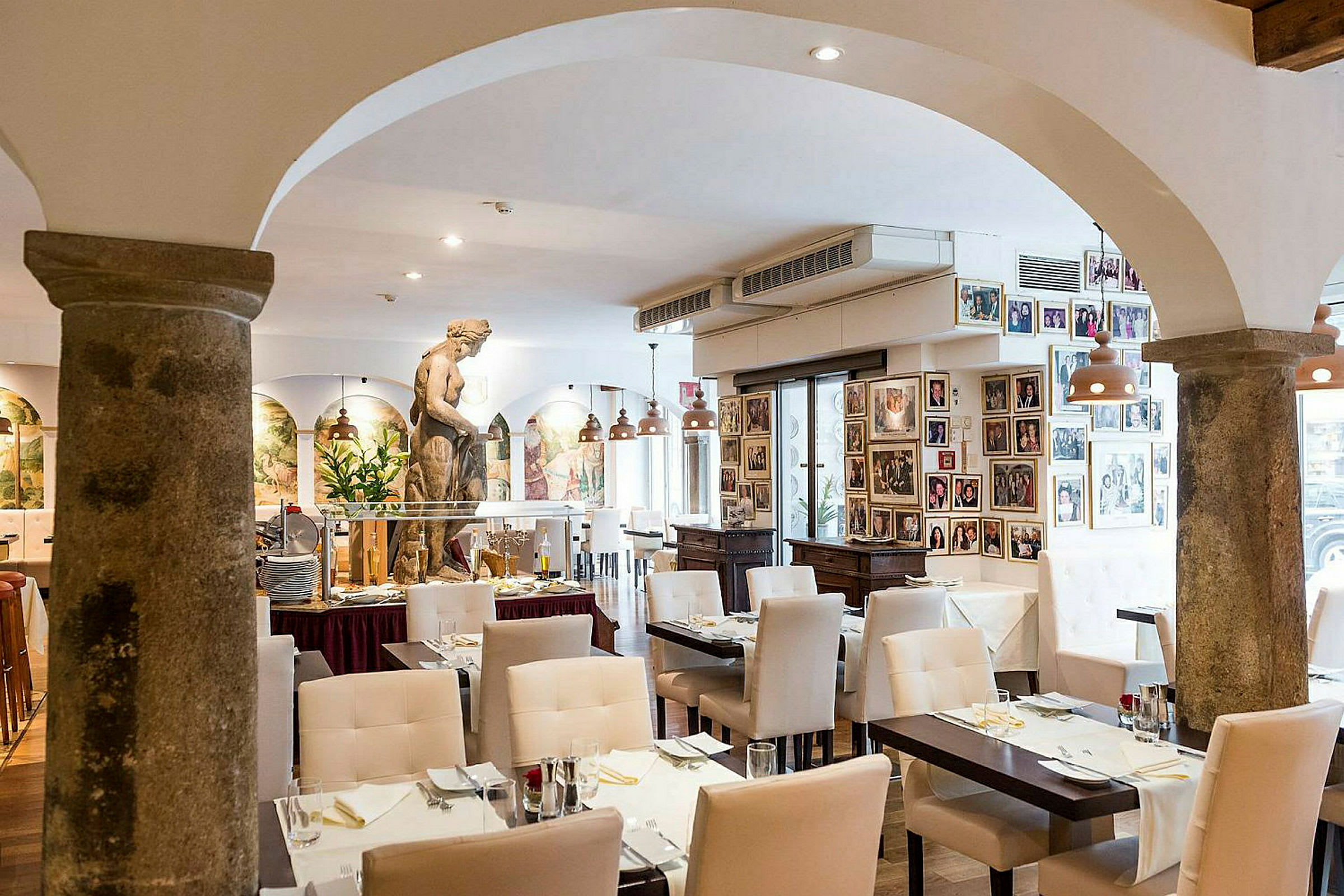 Interiør av en restaurant med hvite stoler, dekkede bord og en skulptur i midten av rommet. (AI-generert tekst)