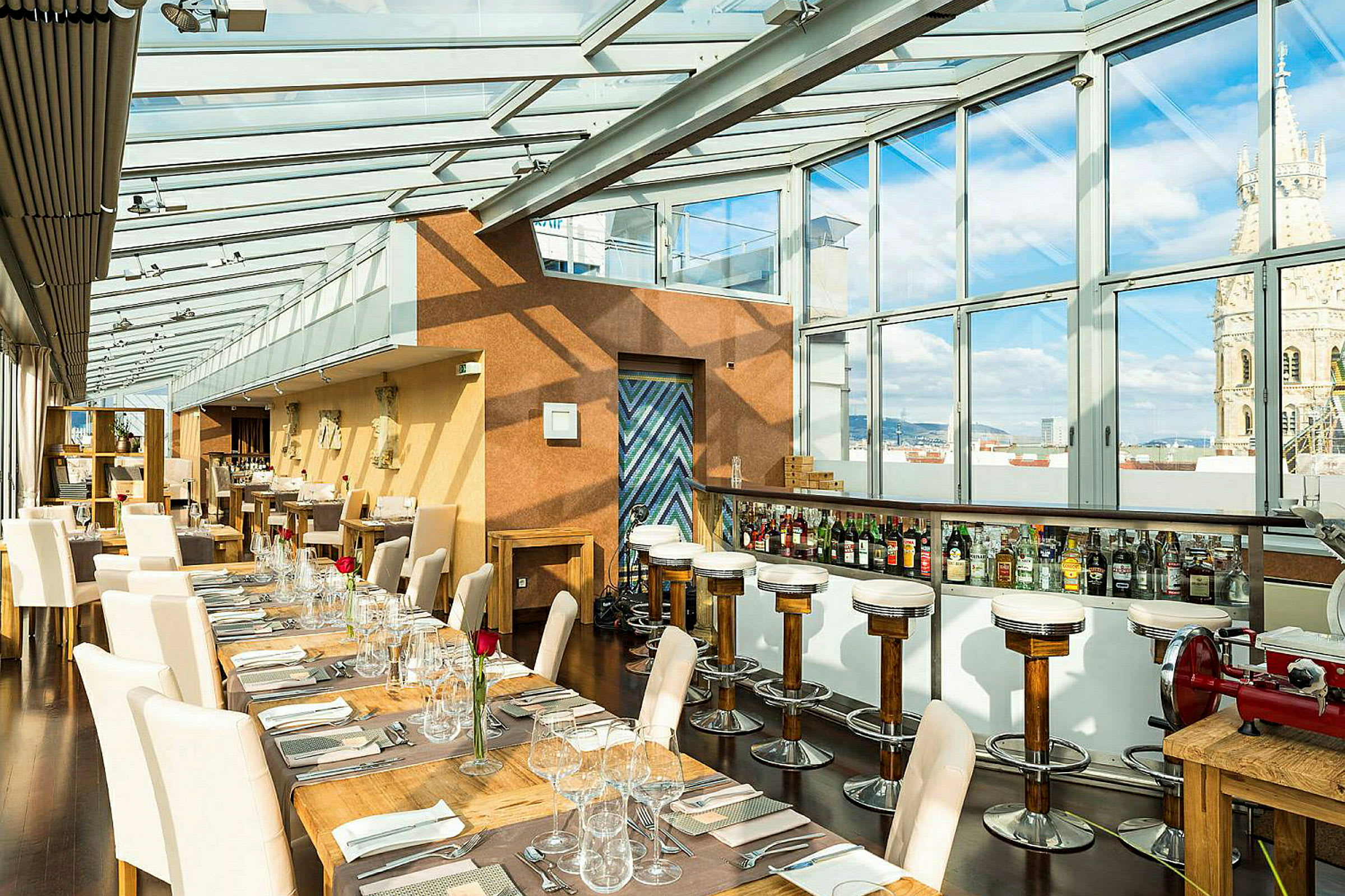 Interiør av en restaurant med glassvegger og -tak som slipper inn naturlig lys. Bord og stoler er elegant oppstilt med duker og glass. (AI-generert tekst)