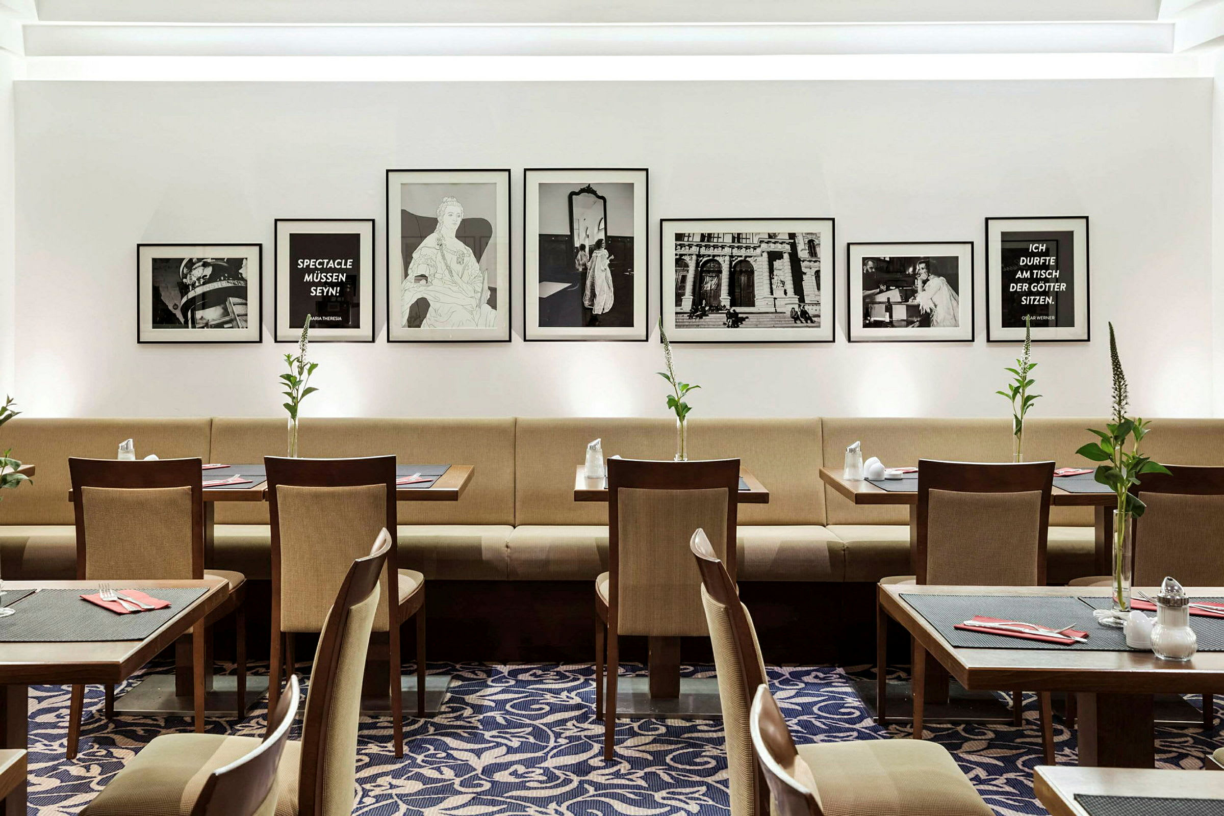 Interiør av en restaurant med bord, stoler og en sofalignende sitteplass langs veggen. Veggen er dekorert med innrammede bilder og tekster. (AI-generert tekst)