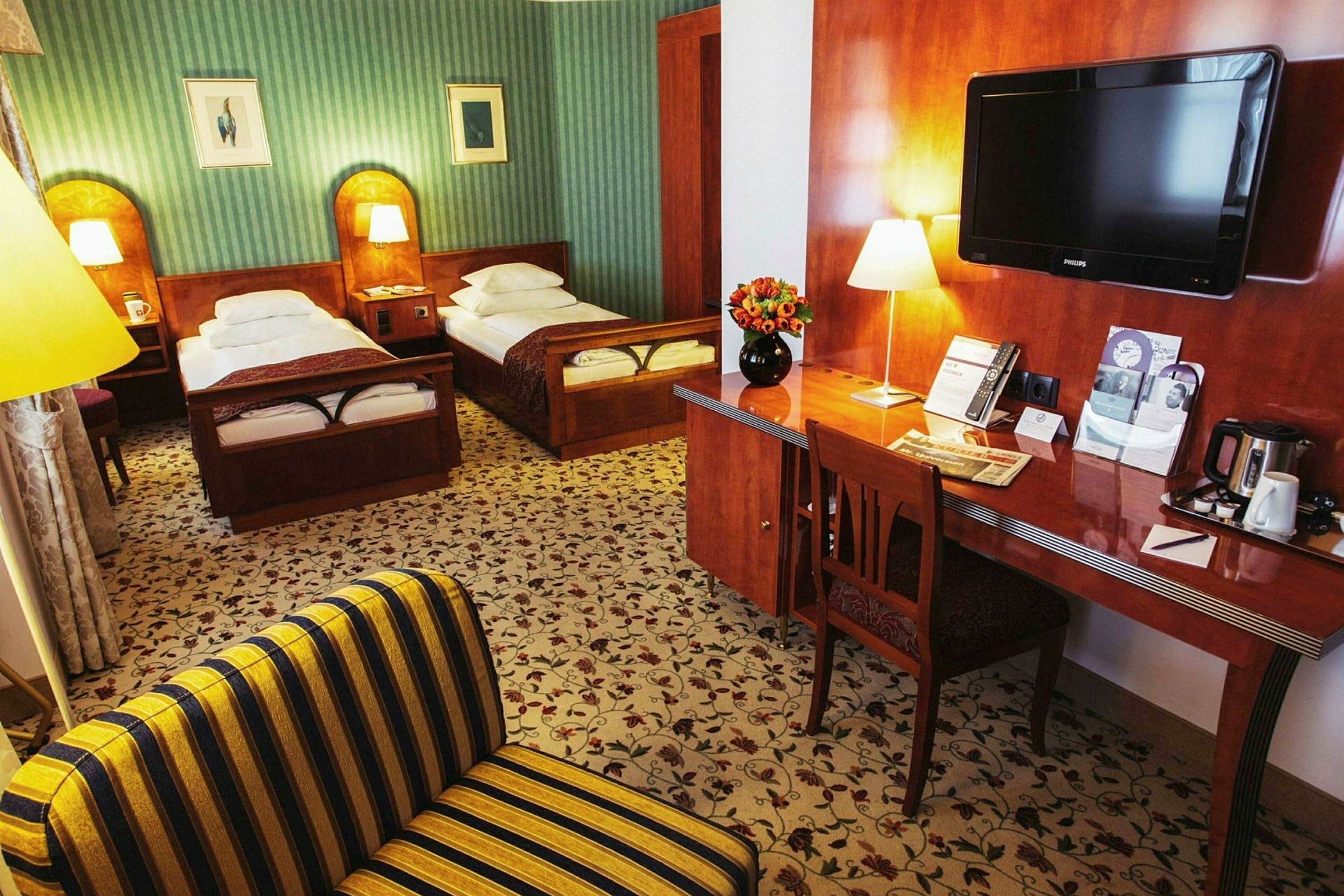 Et hotellrom med to enkeltsenger, en skrivebord med blomster og en TV. (AI-generert tekst)